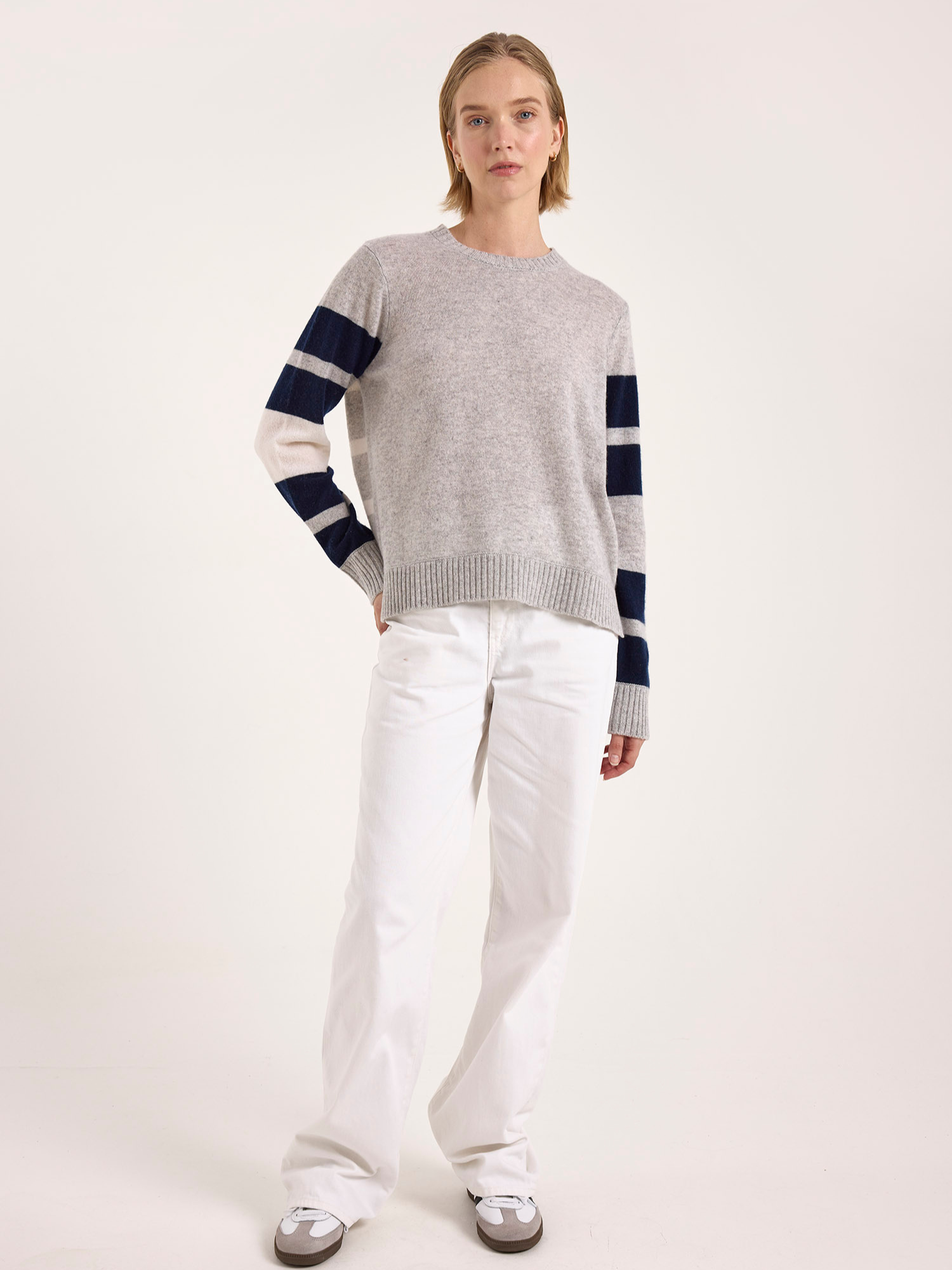 Woman wearing a gray cashmere sweater with blue and white striped sleeves on a white background