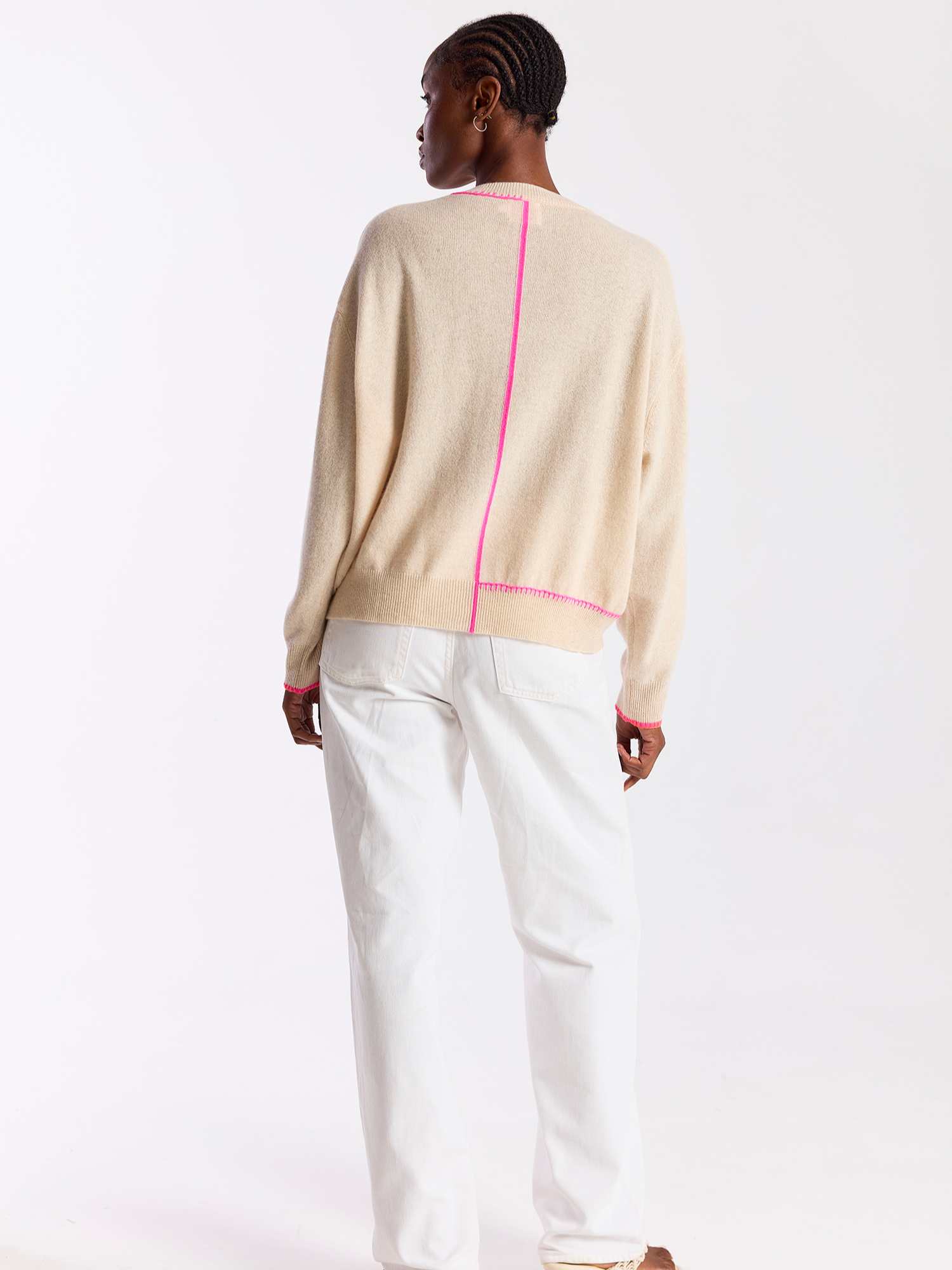 Person wearing a beige sweater with pink accents and white pants on a white background