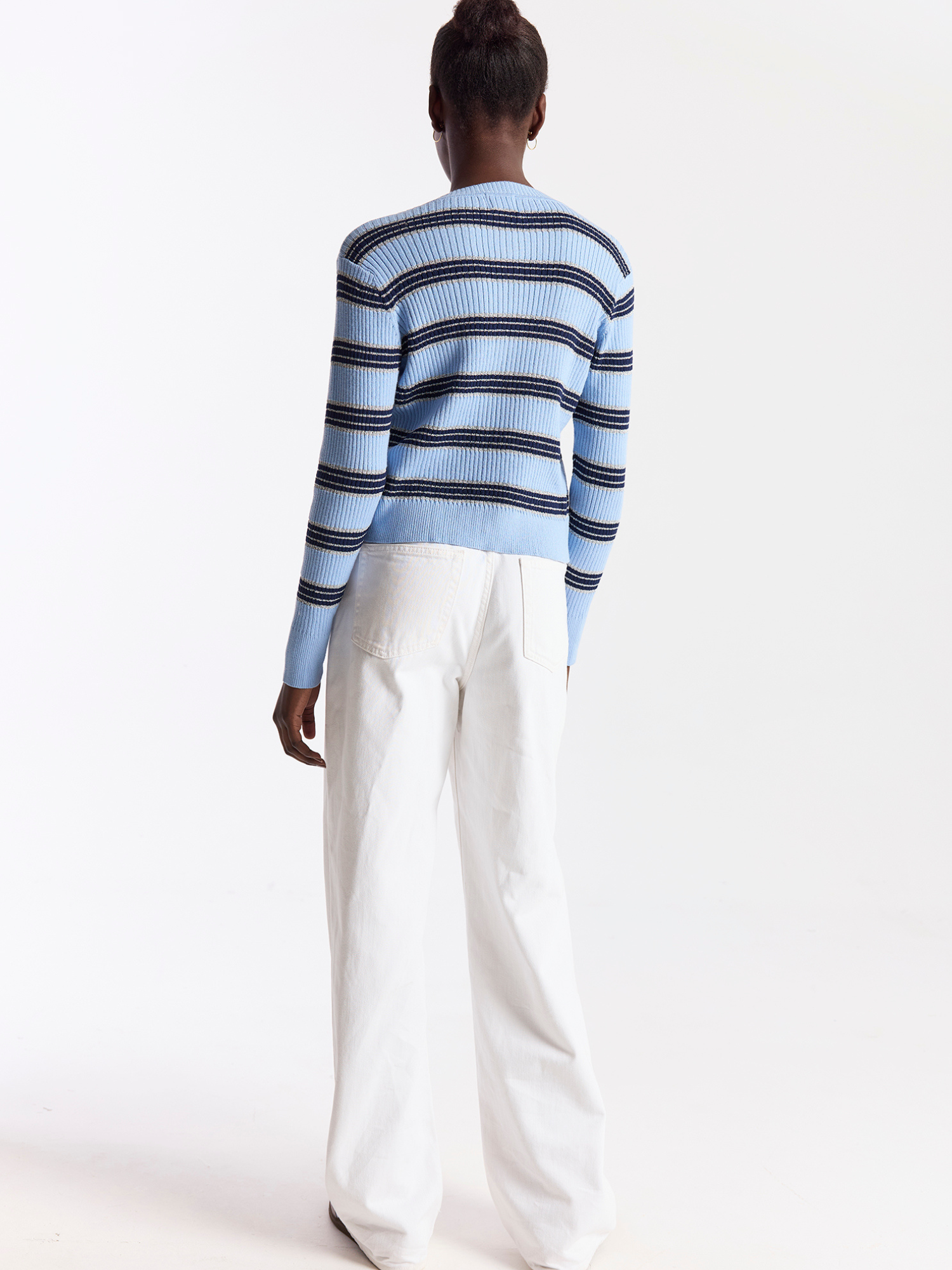 Person wearing a blue and white striped sweater with white pants on a light gray background