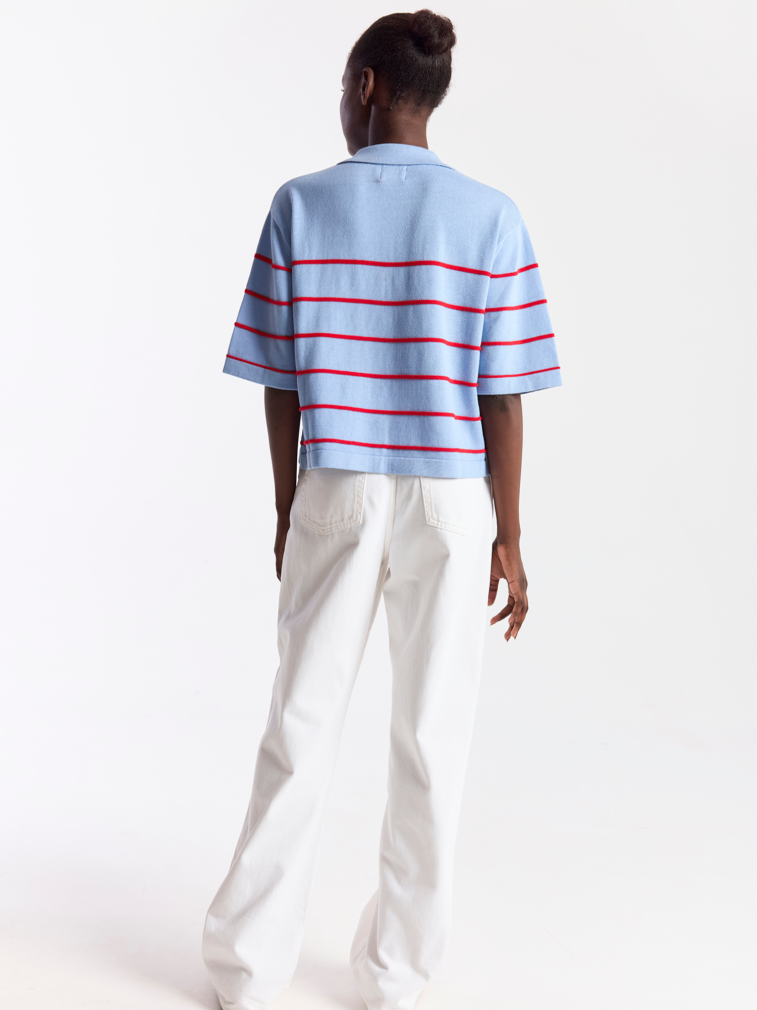 Person wearing a light blue and red striped shirt with white pants on a white background