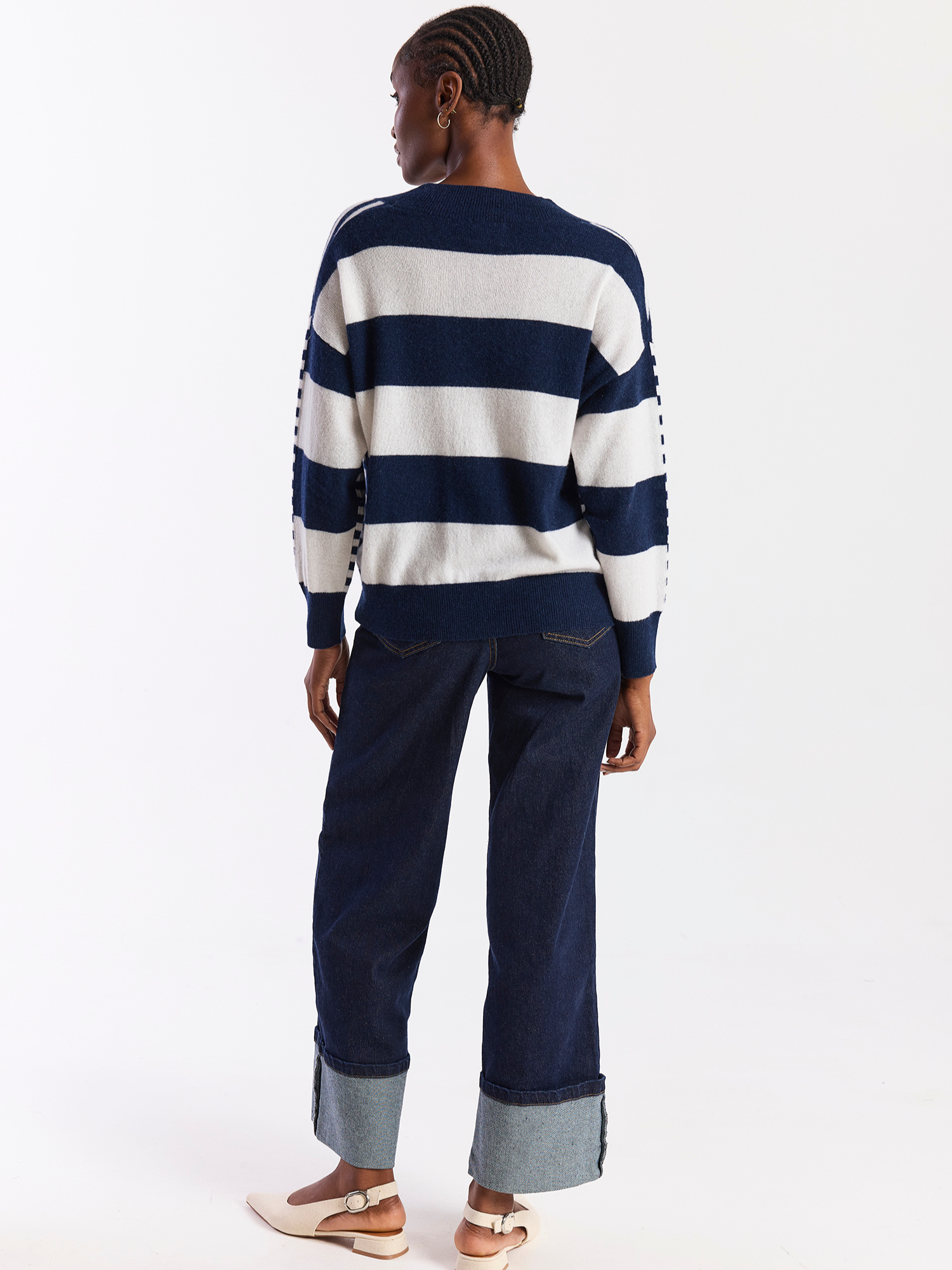 Person wearing a navy and white striped sweater with rolled-up blue pants on a white background