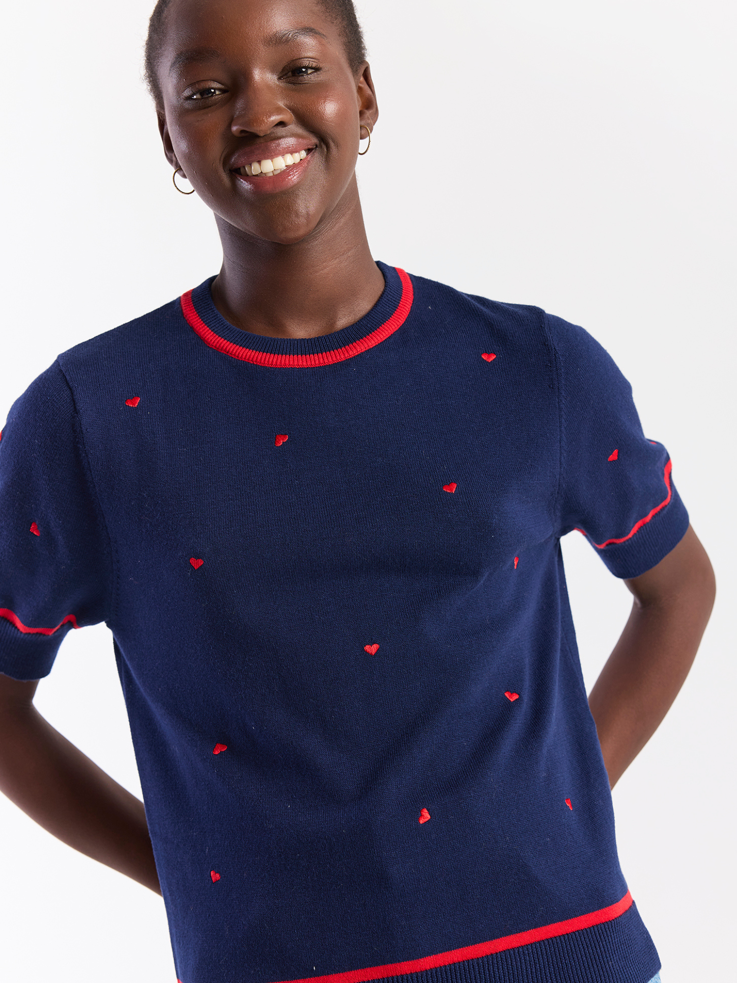 Woman wearing a navy sweater with red heart patterns on a white background