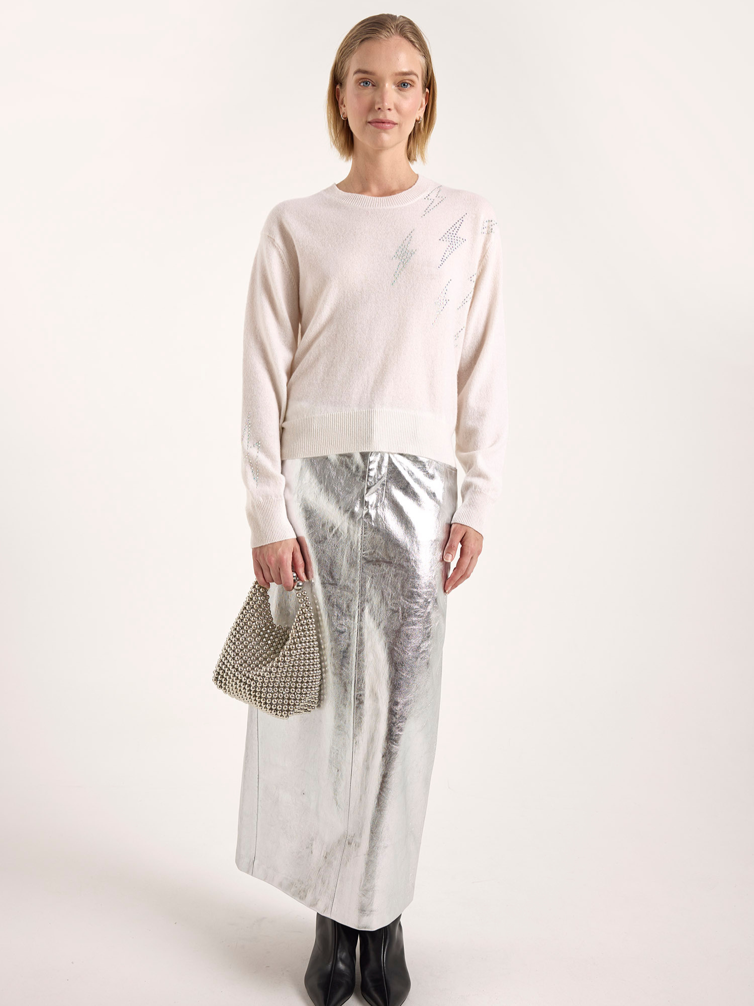 Woman wearing a light pink sweater and silver skirt with a white background