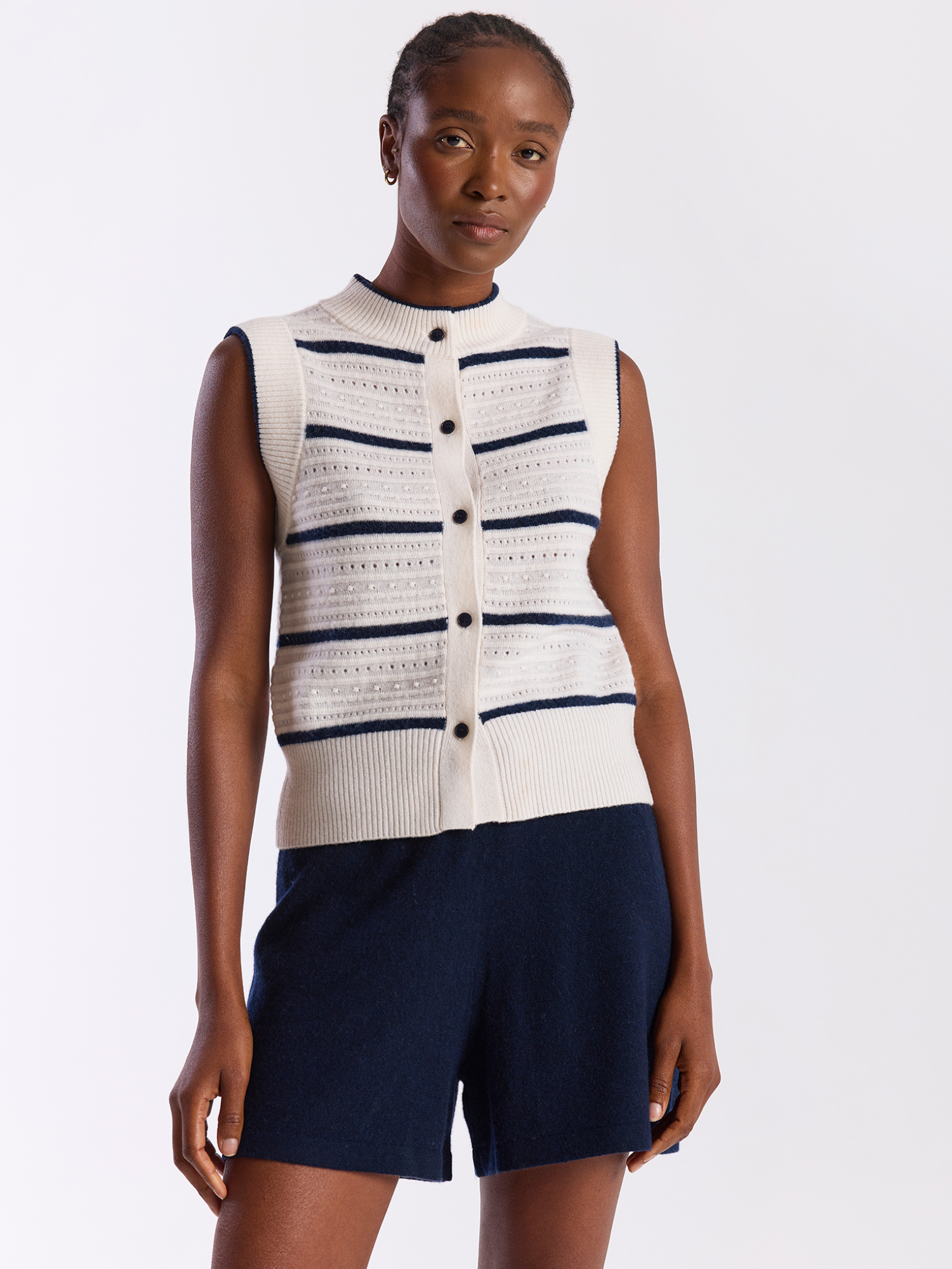 Woman wearing a sleeveless striped sweater vest and navy shorts on a white background