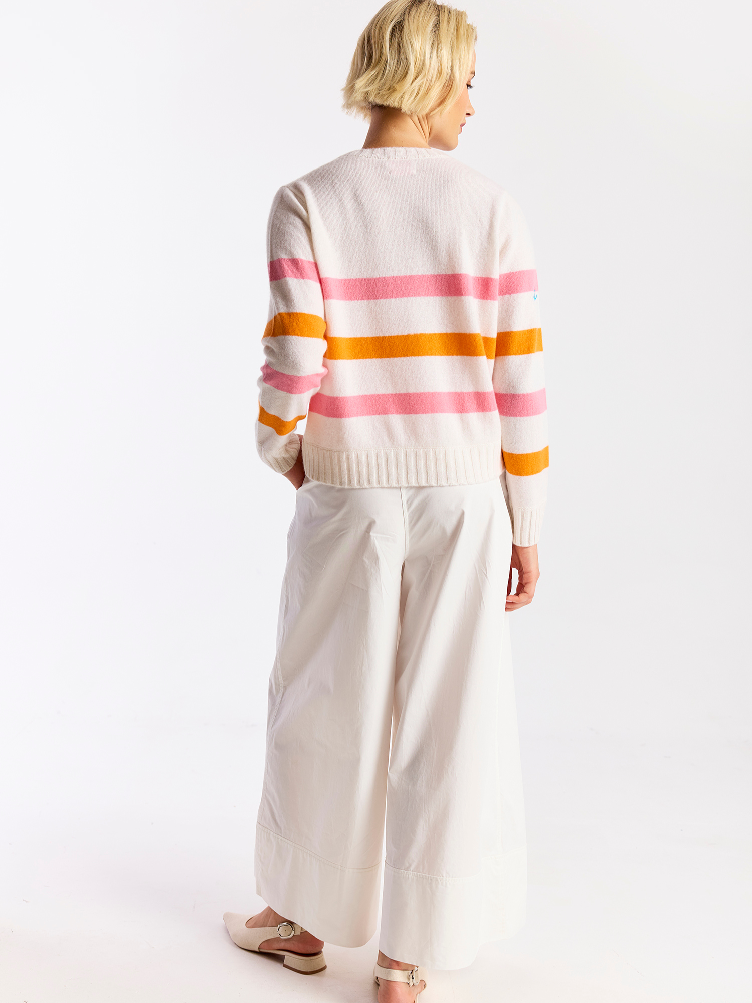 Woman wearing a striped cashmere sweater with pink and orange horizontal stripes on a white background