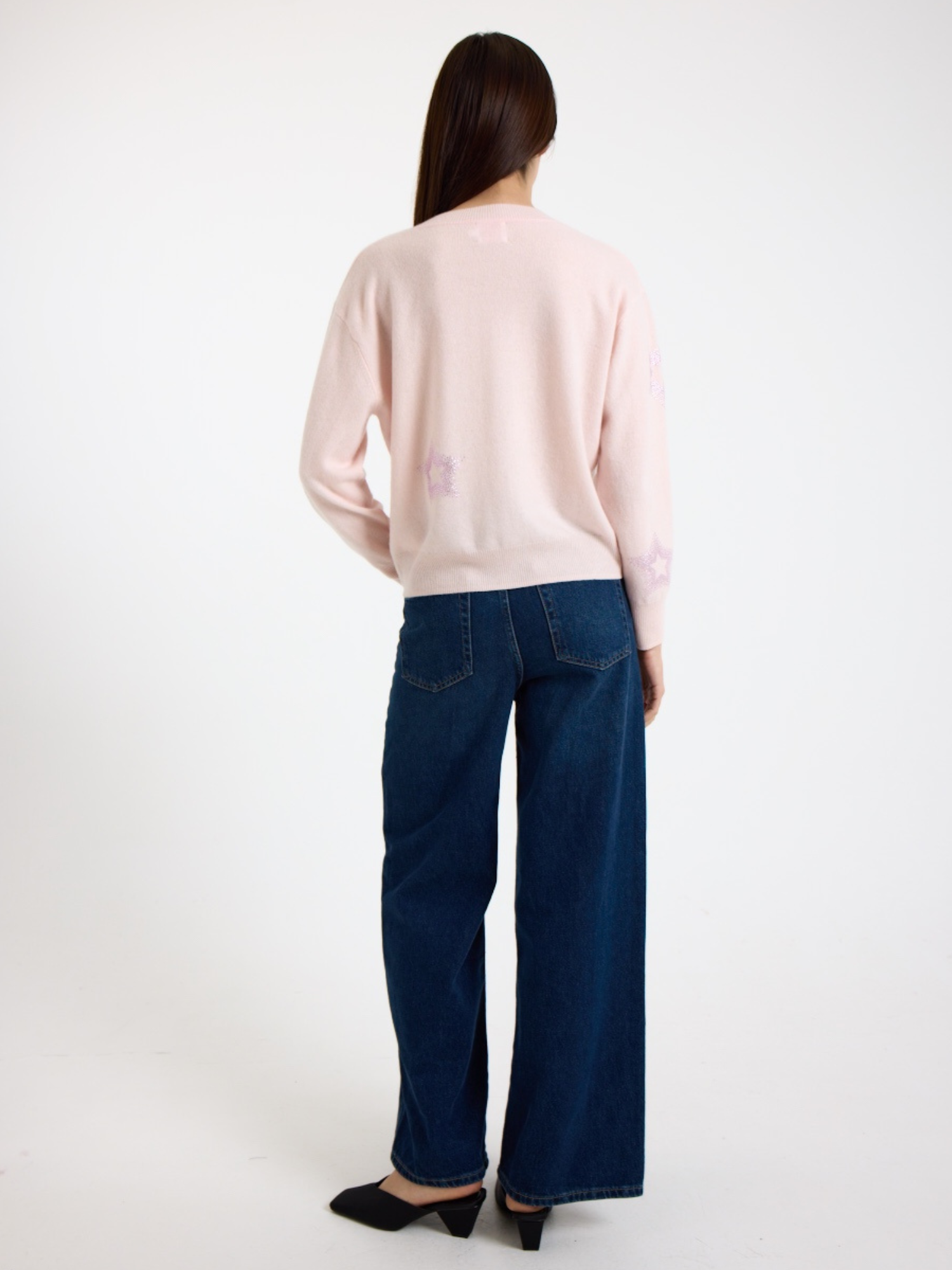 Person wearing a light pink sweater and blue jeans on a white background