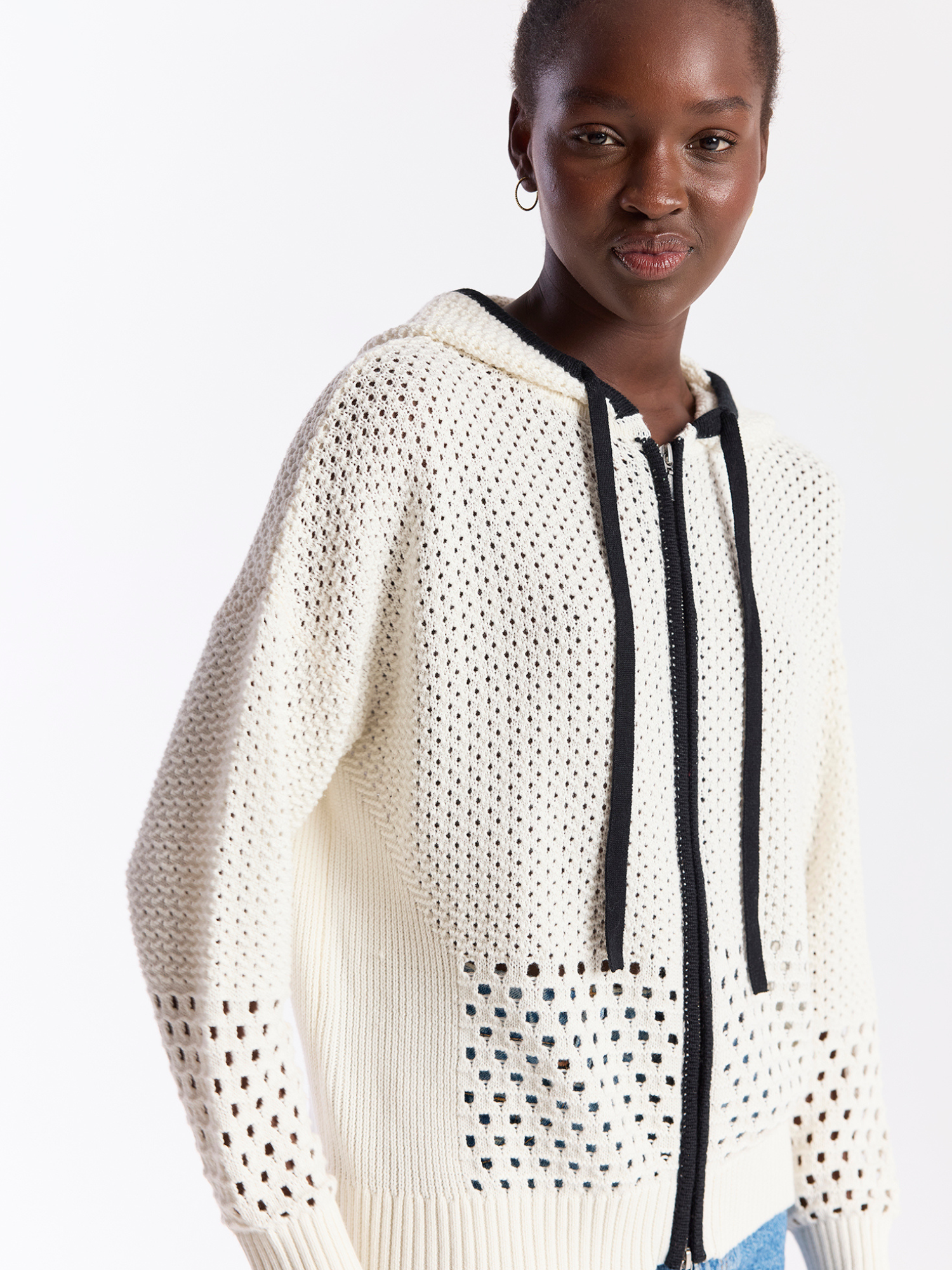 Person wearing a white textured sweater with black accents on a light gray background