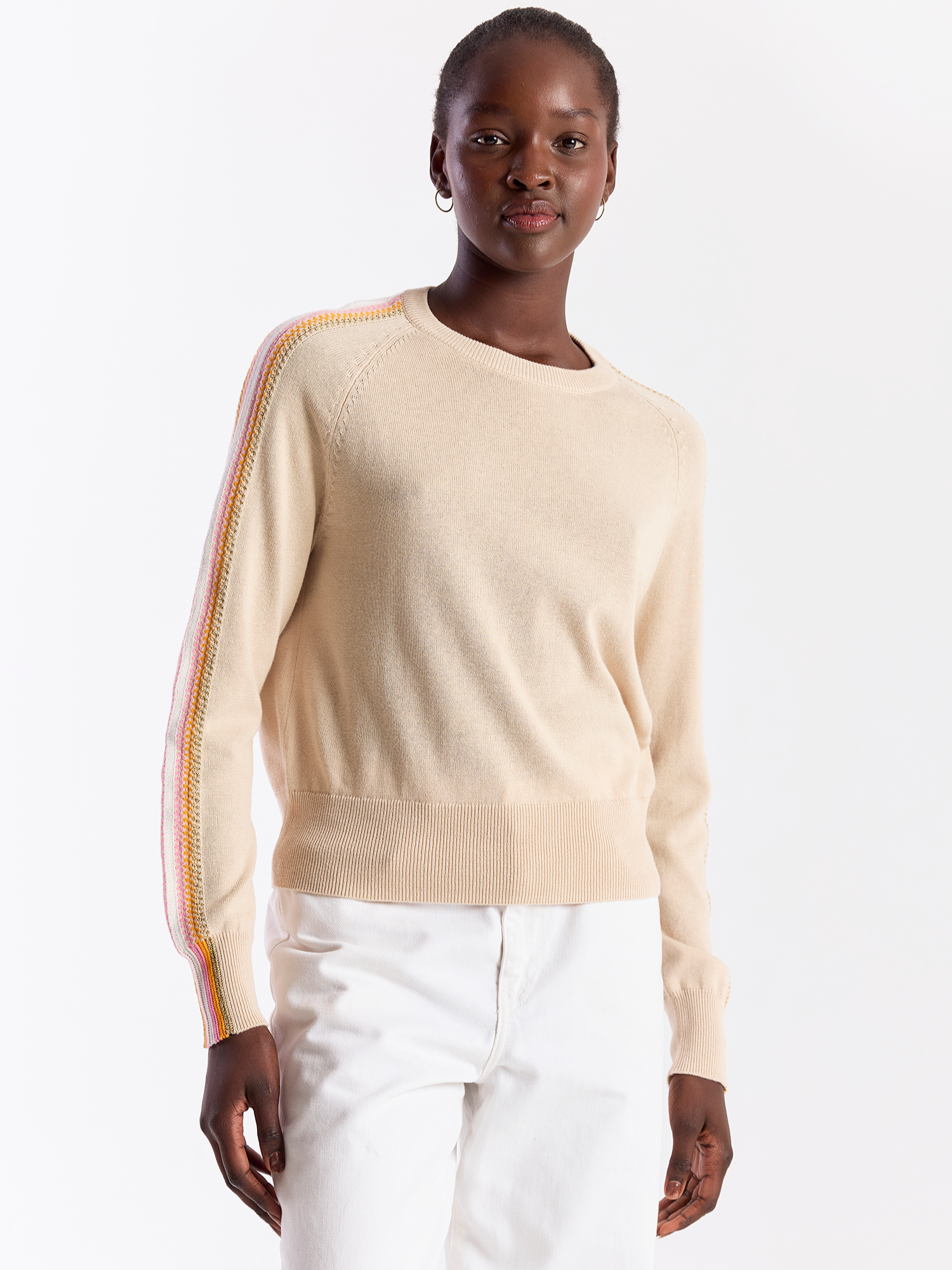 Woman wearing a beige sweater with colorful stripes on a white background
