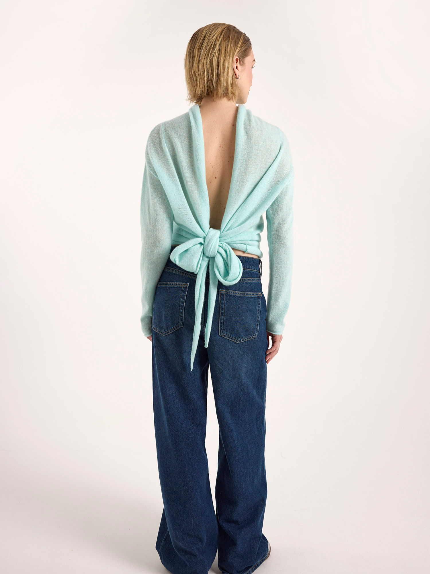 Person wearing a light blue cardigan with a tie detail over a white background