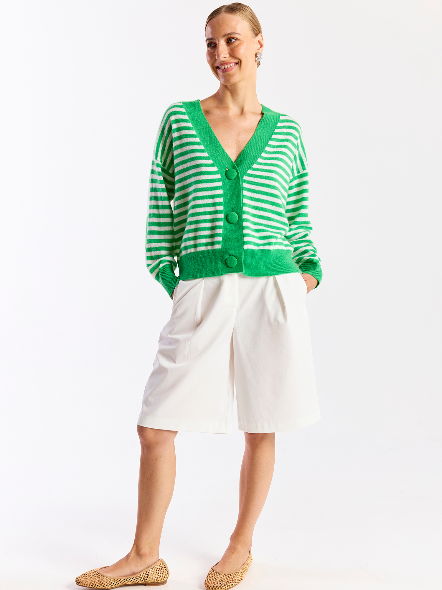 Woman wearing a green and white striped cardigan with a white skirt on a white background