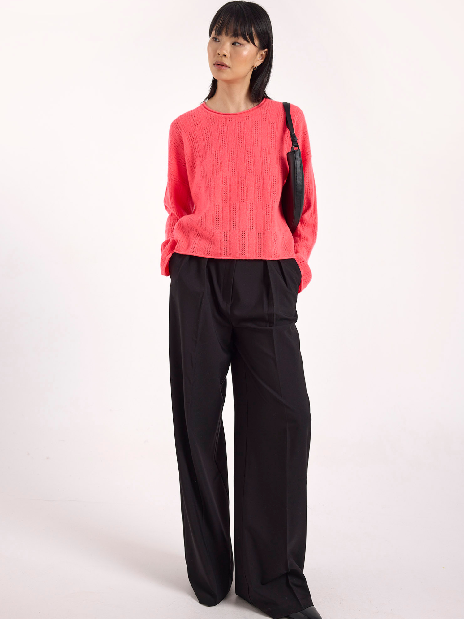 Woman wearing a pink sweater and black pants on a white background