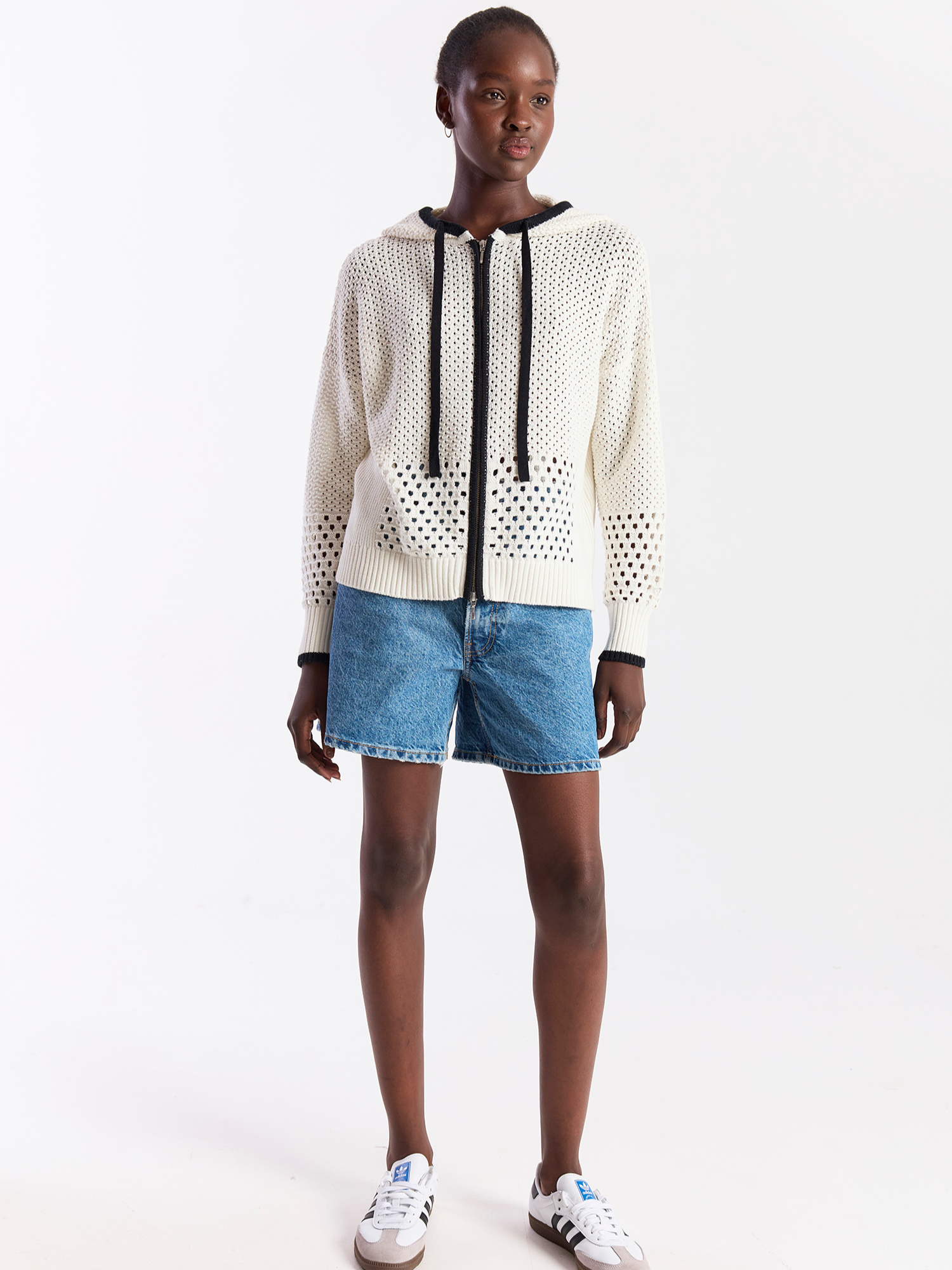Person wearing a white perforated hoodie with black drawstrings and blue denim shorts on a white background