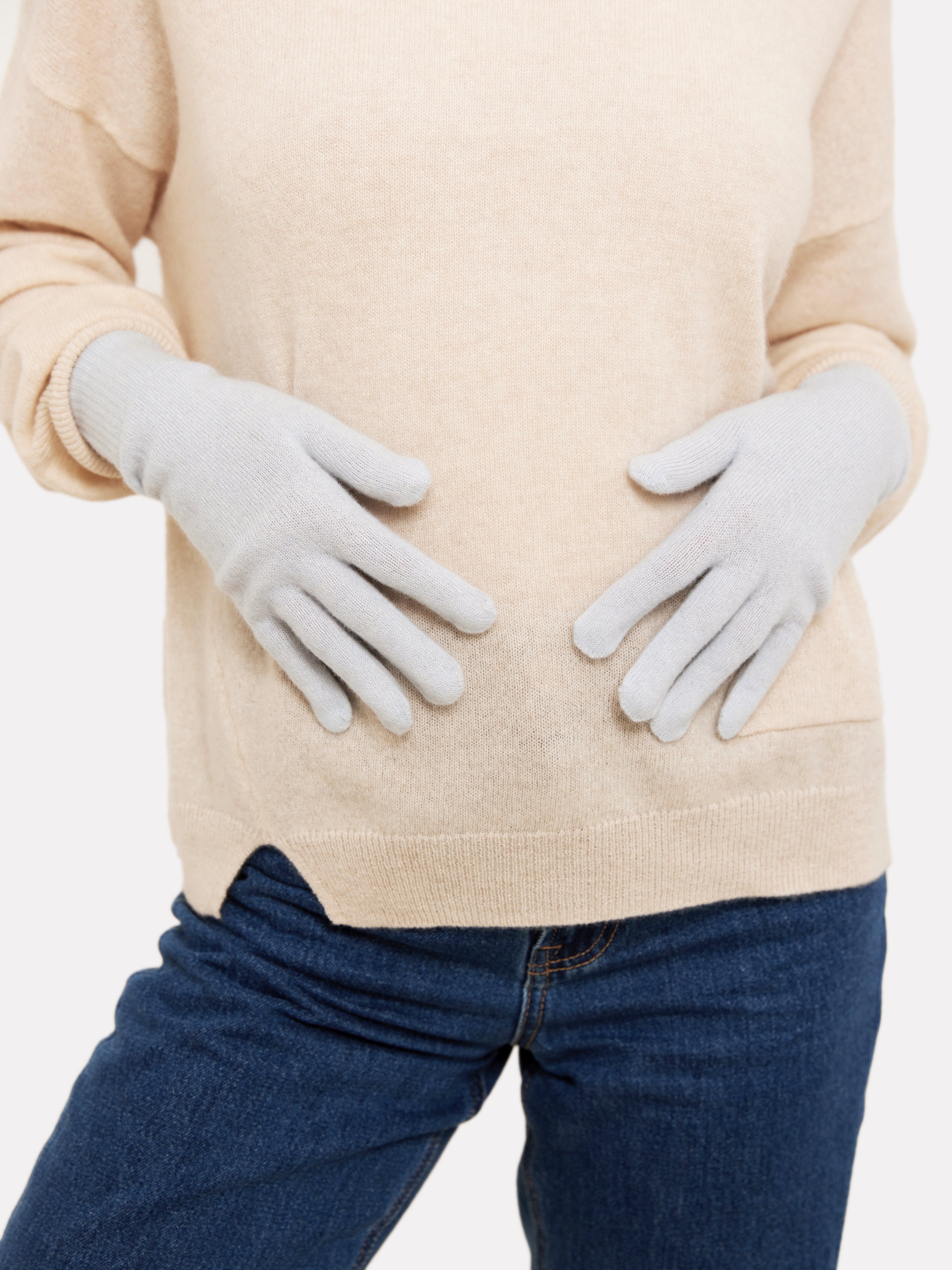 Person wearing light blue gloves and a beige sweater on a white background