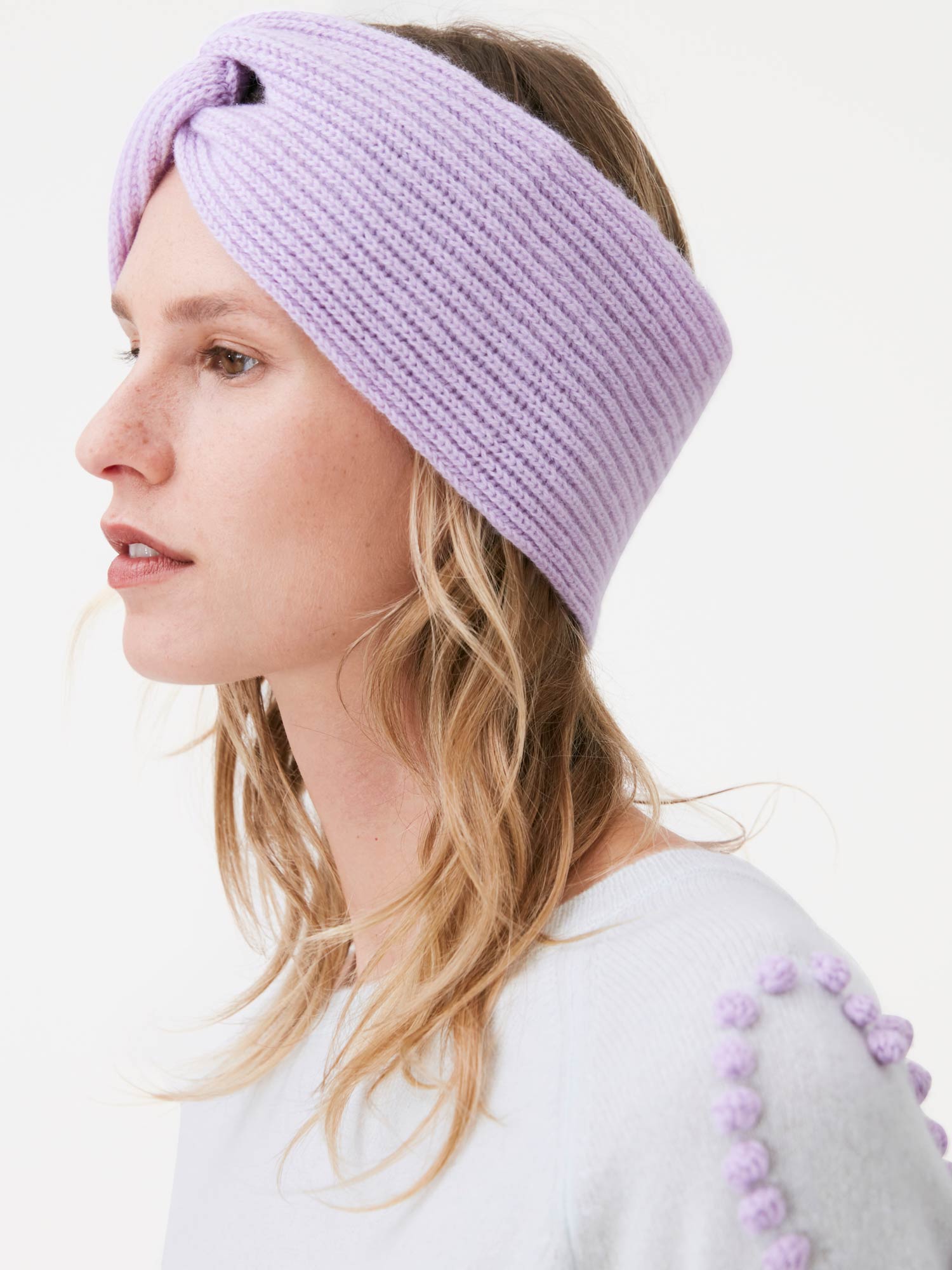 Woman wearing a light purple knitted headband with a plain background