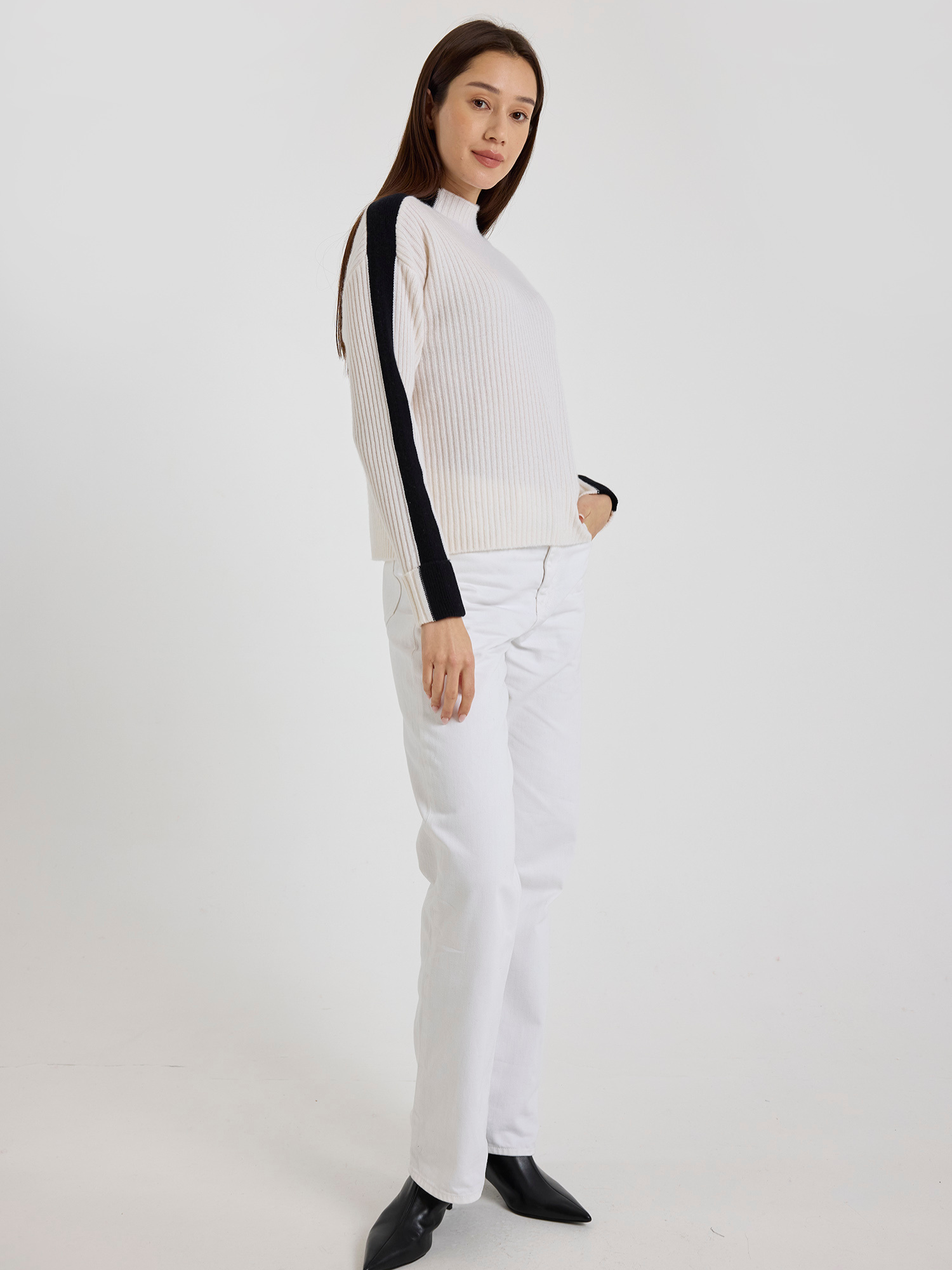 Woman wearing a white ribbed sweater with black stripe sleeves and white jeans pants on a white background