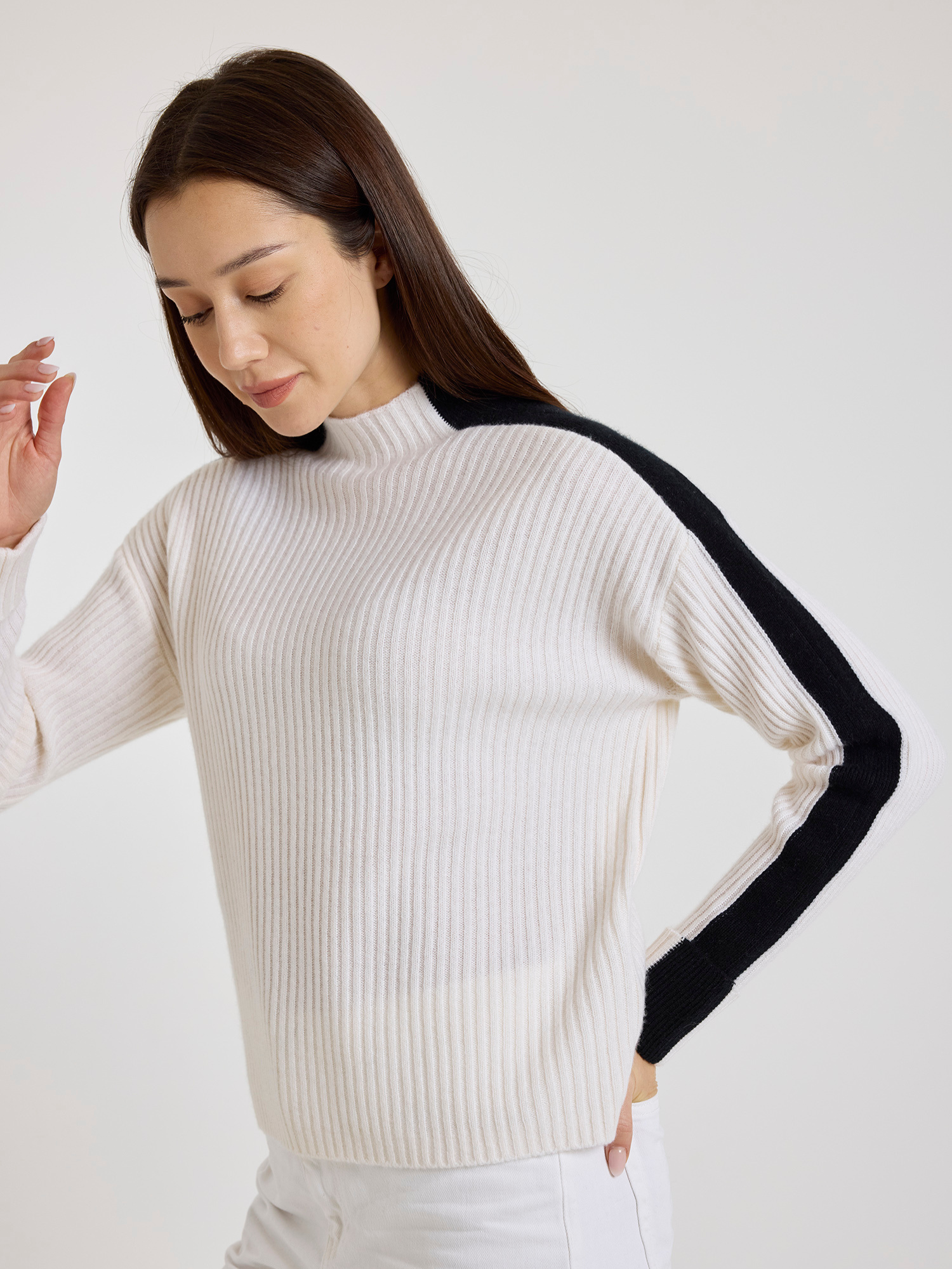 Woman wearing a white ribbed sweater with black stripe sleeves and white jeans pants on a white background