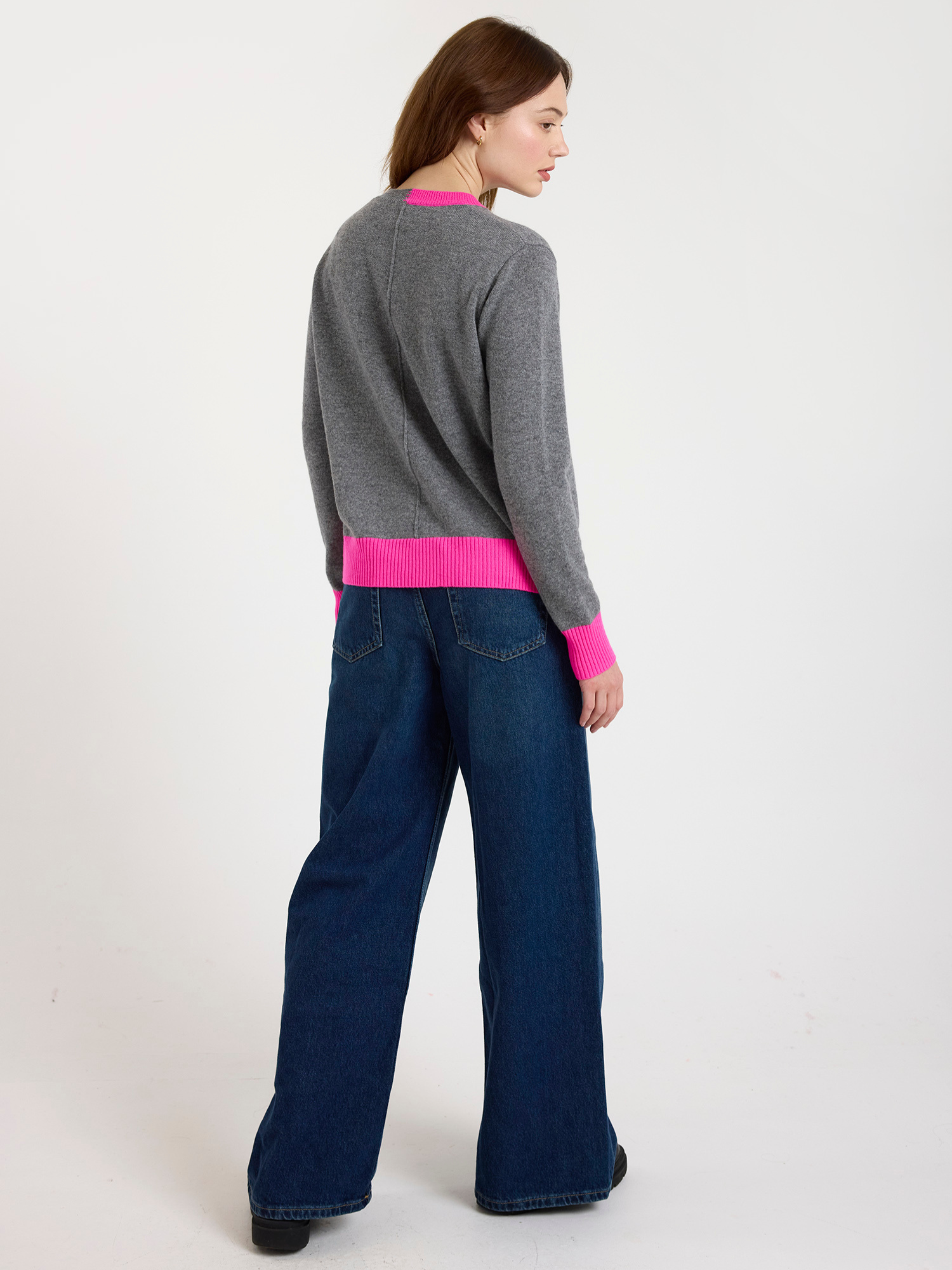 Woman wearing a grey sweater with pink trim and blue jeans on a white background
