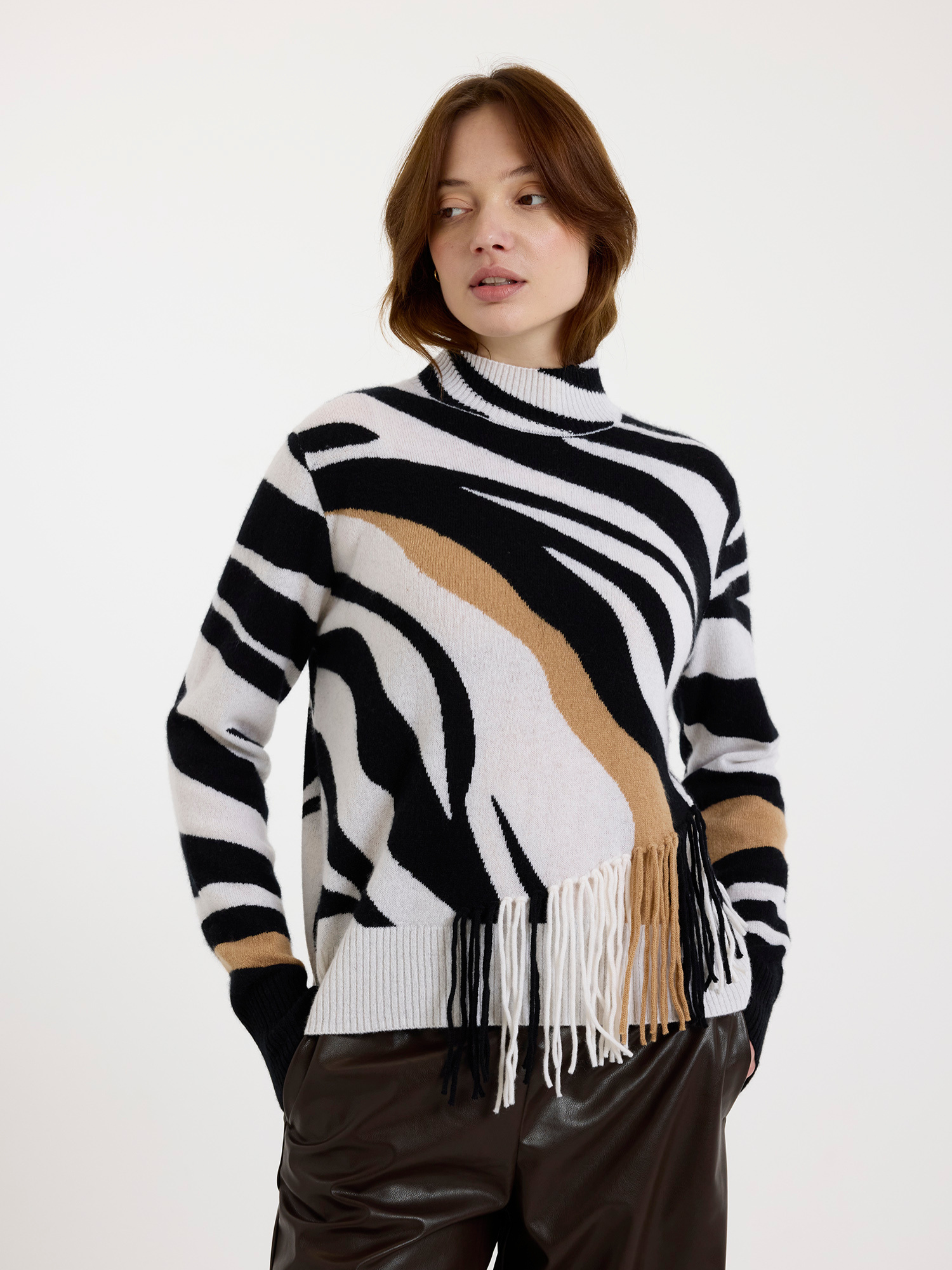 Woman wearing a black and white zebra pattern sweater with fringes on a white background