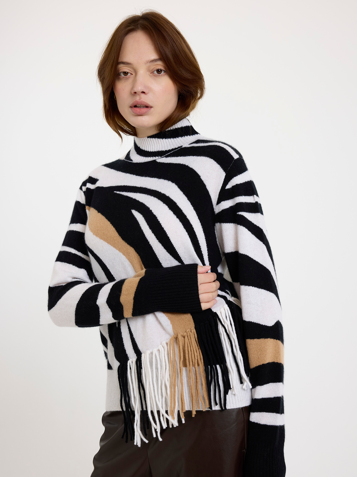 Woman wearing a black and white zebra pattern sweater with fringes and brown leather trousers on a white background