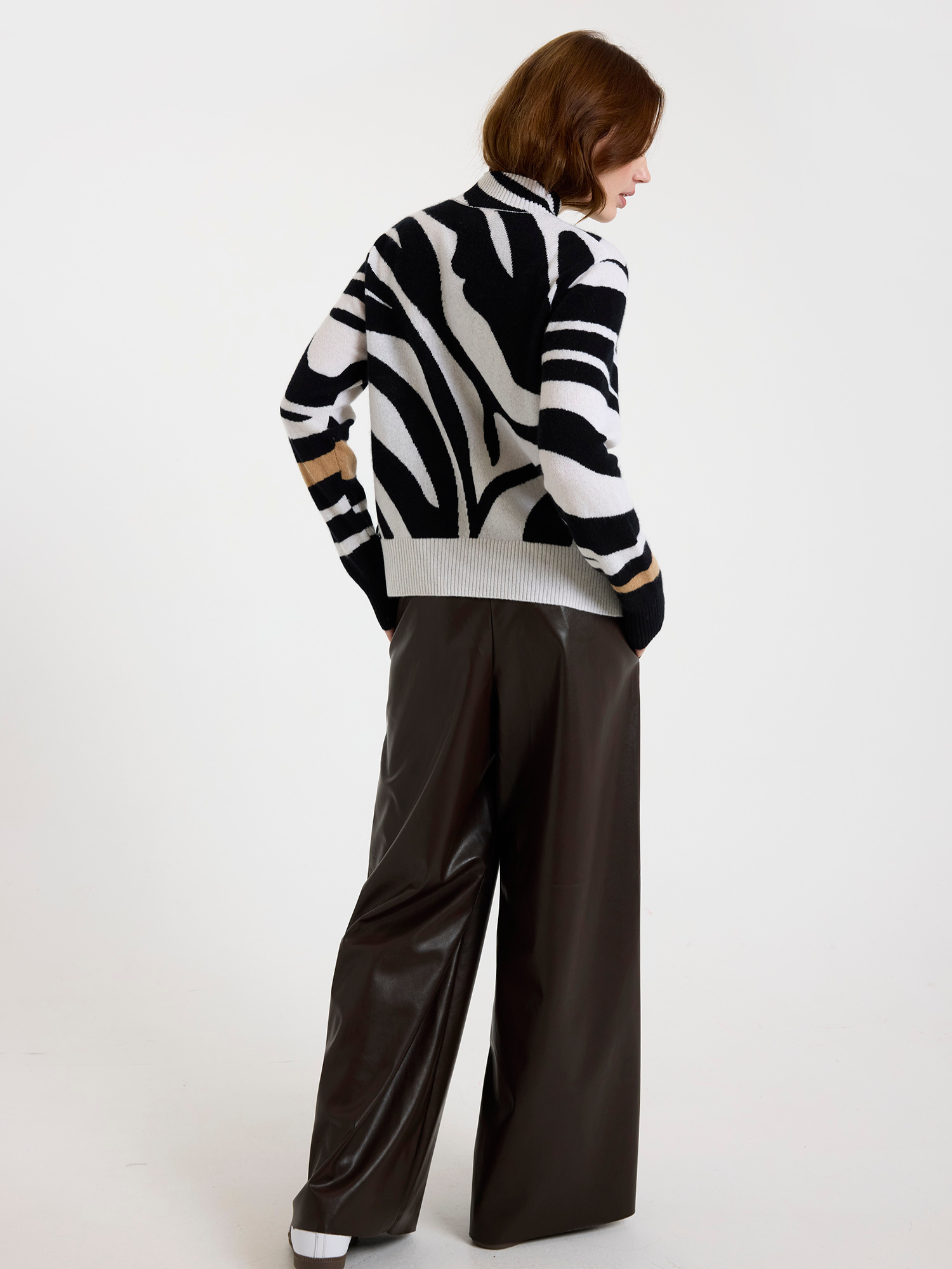 Woman wearing a black and white zebra pattern sweater with fringes and brown leather trousers on a white background