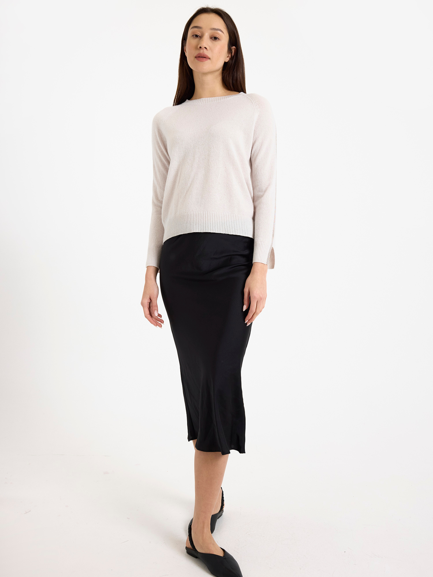 Woman wearing a light grey sweater with glitz detail down the arm with a black skirt on a white background
