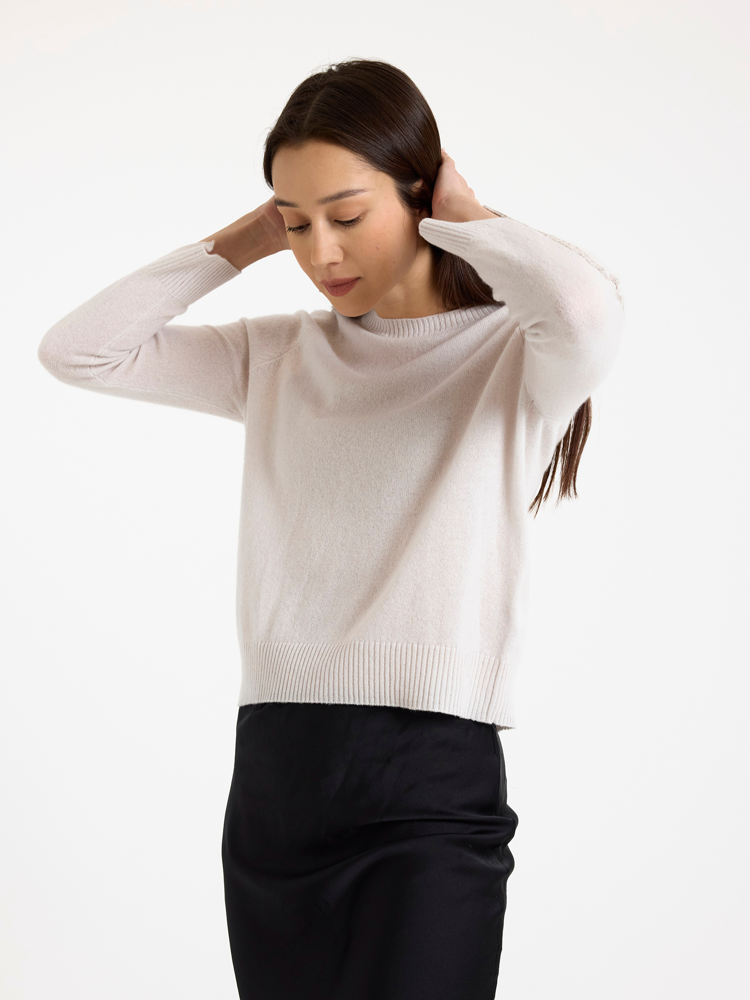 Woman wearing a light grey sweater with glitz detail down the arm with a black skirt on a white background