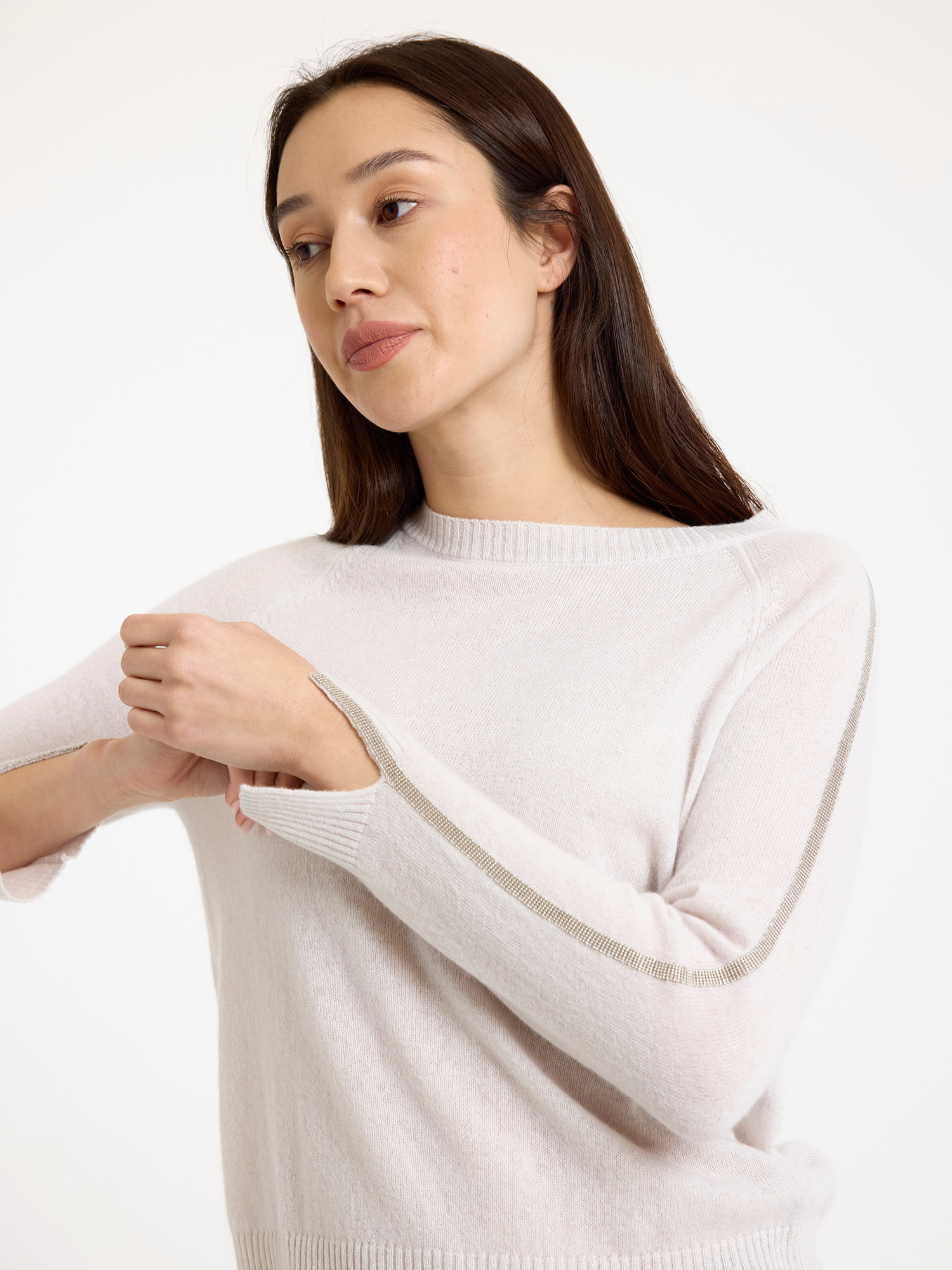 Woman wearing a light grey sweater with glitz detail down the arm on a white background