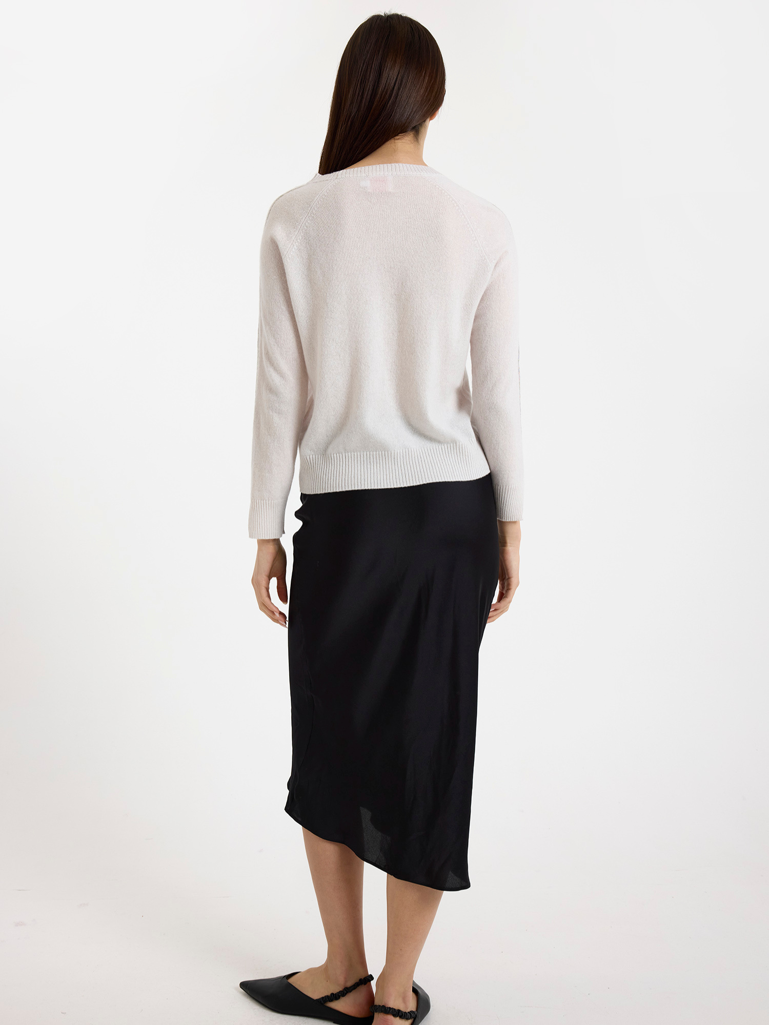 Woman wearing a light grey sweater with glitz detail down the arm with a black skirt on a white background