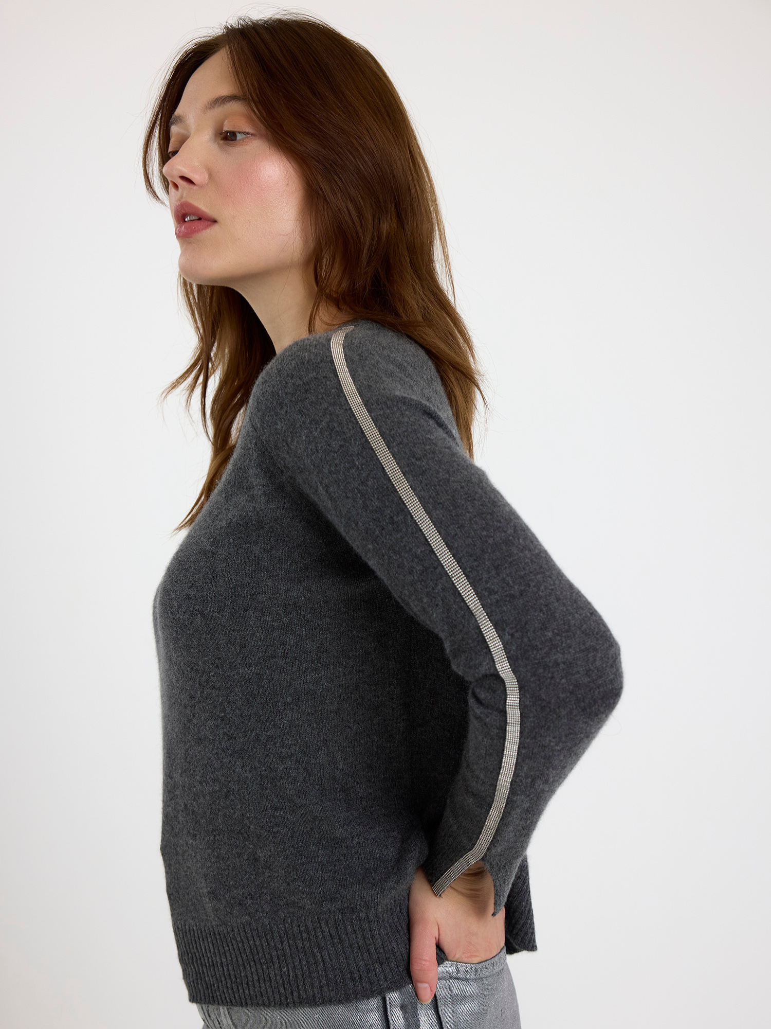 Woman wearing a grey sweater with glitz detail down the arm on a white background