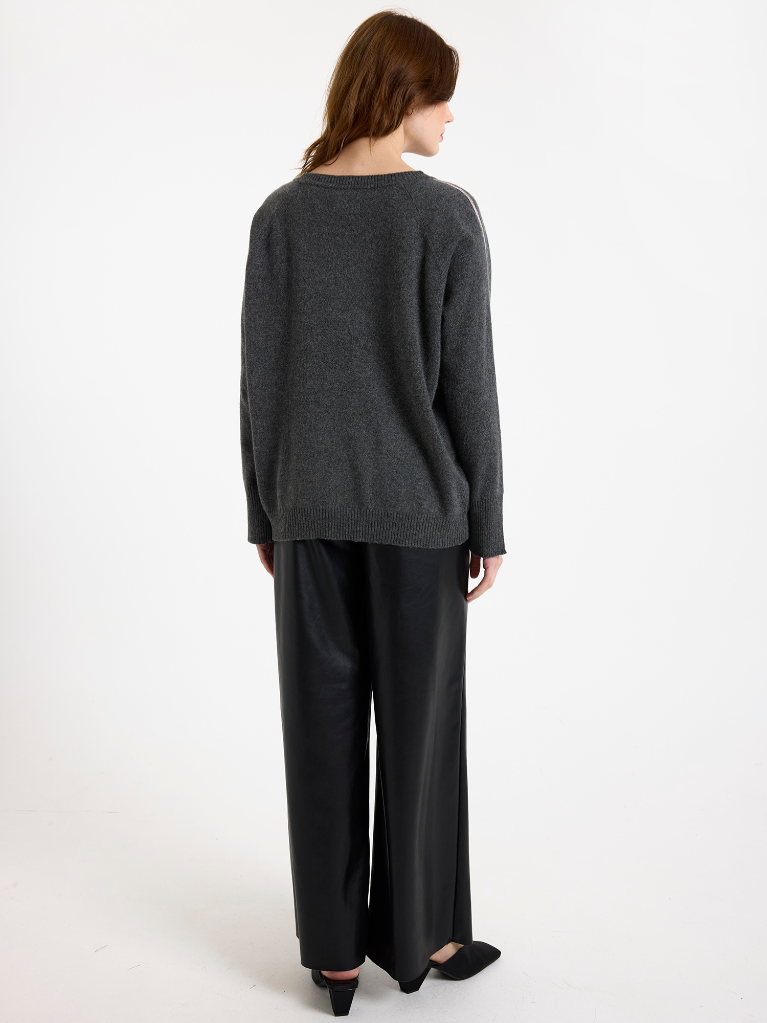 Woman wearing a grey sweater with glitz detail down the arm and black wide-leg pants on a white background
