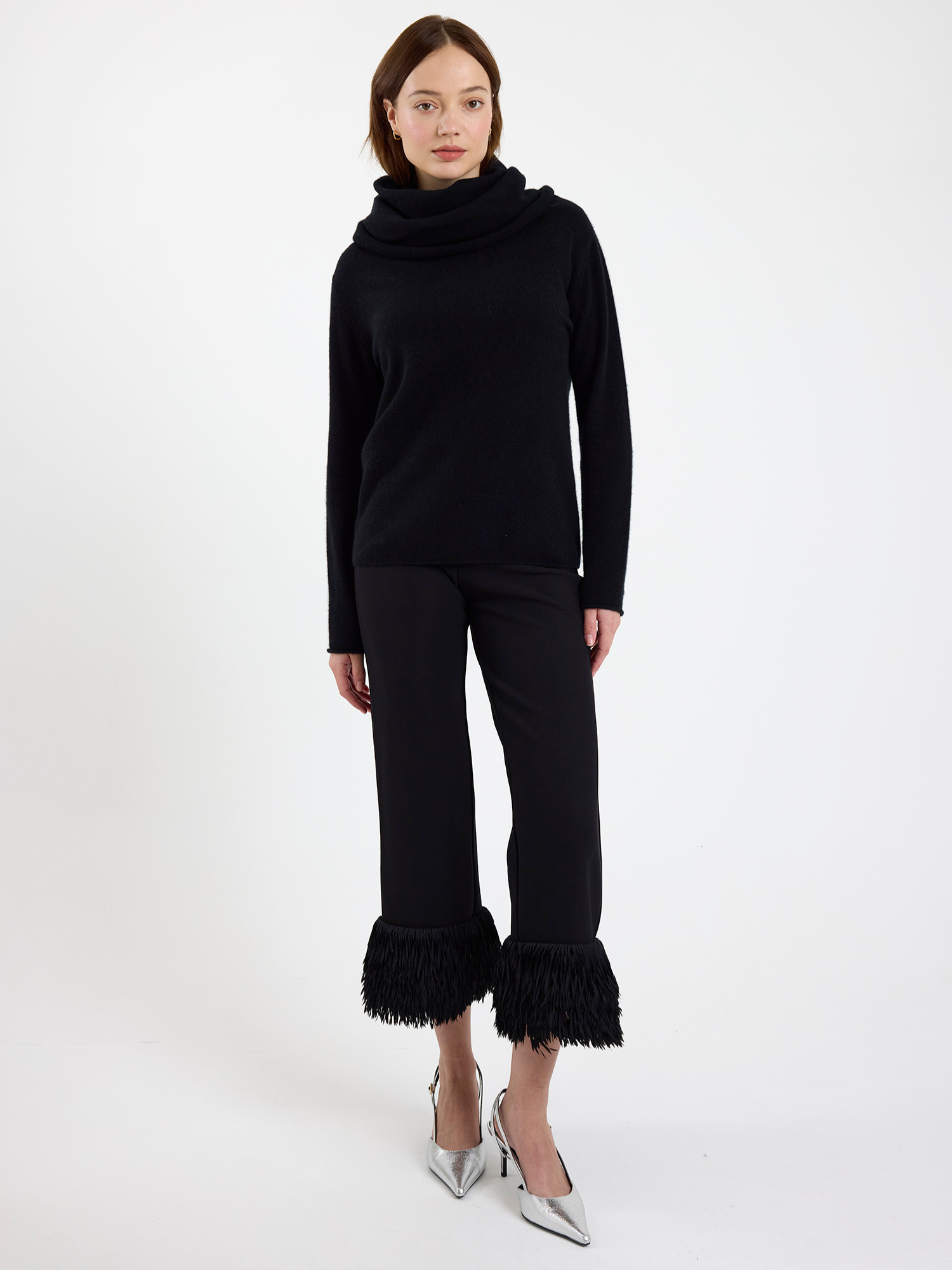 Woman wearing a black cowl-neck sweater with ruffled pants on a white background
