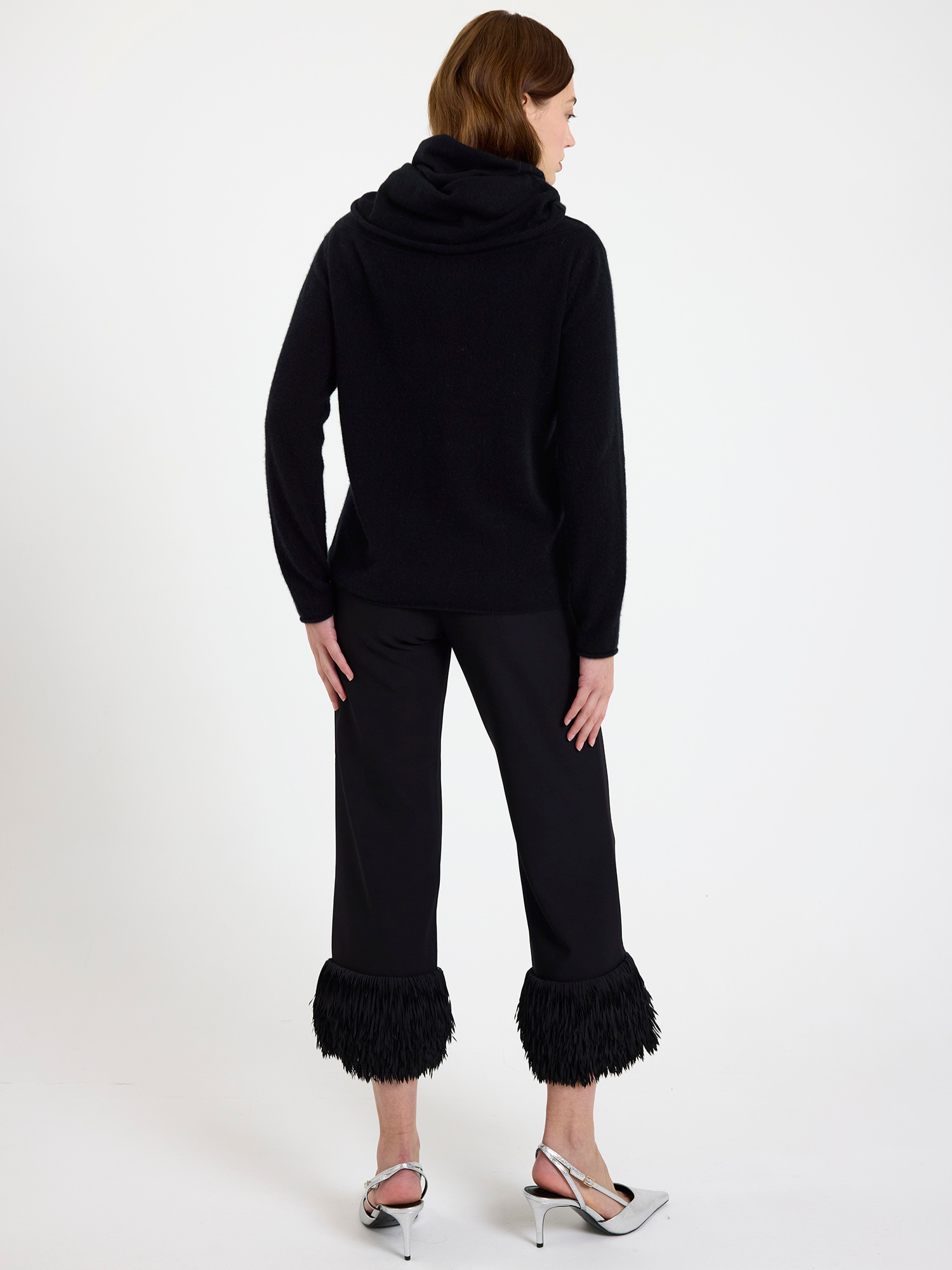Woman wearing a black cowl-neck sweater with ruffled pants on a white background