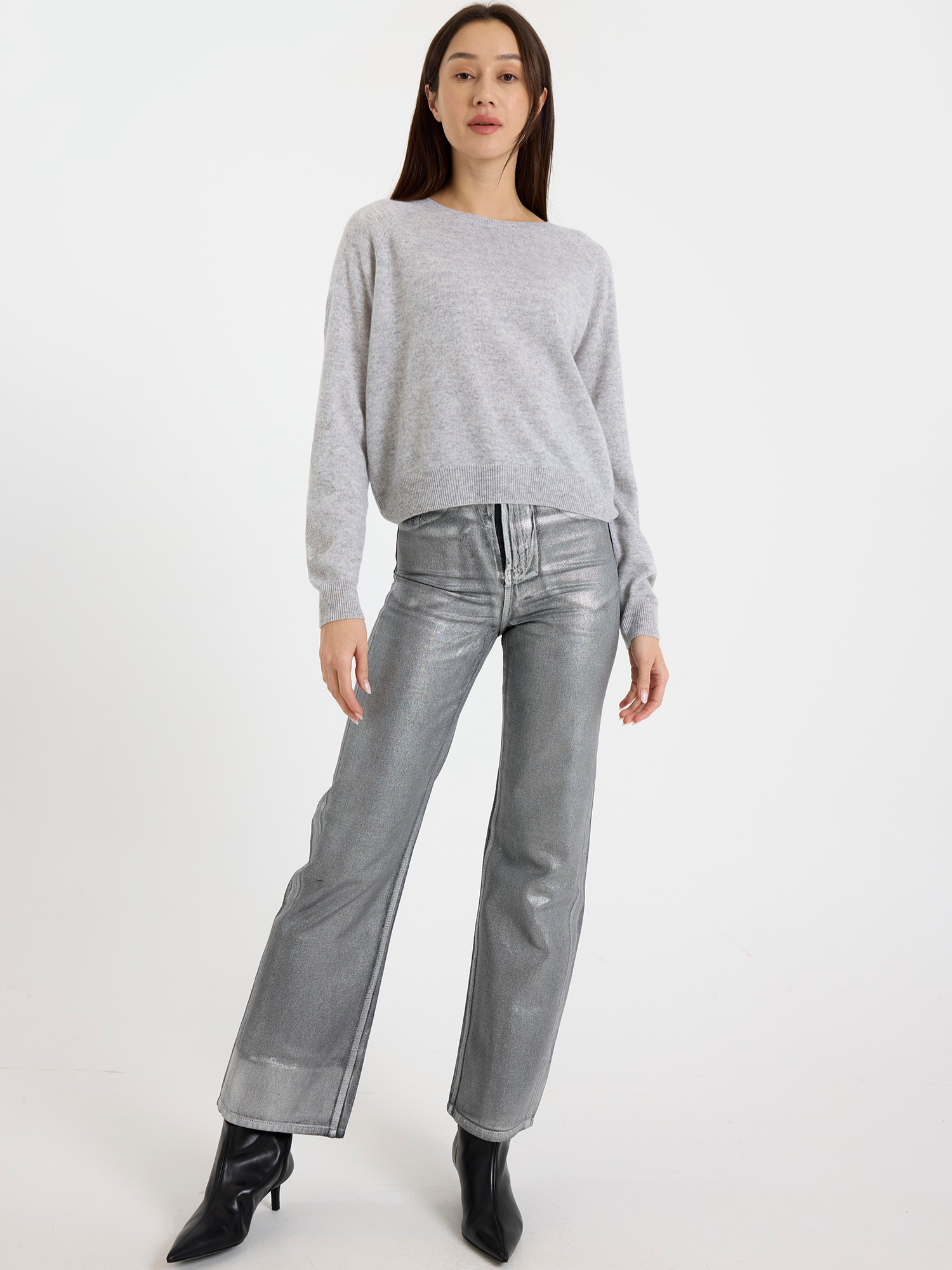 Woman wearing a grey sweater with star detail and silver jeans on a white background