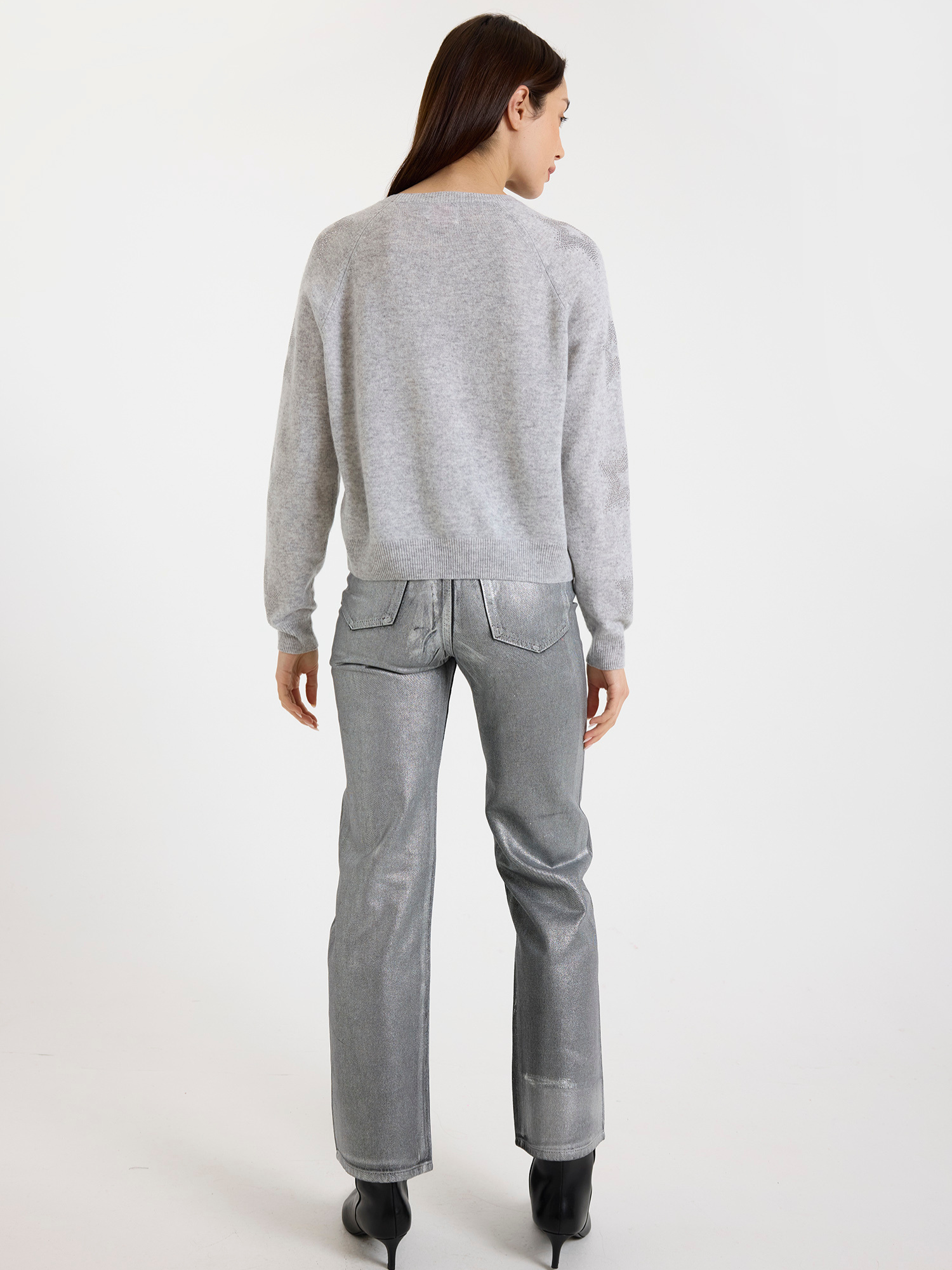 Woman wearing a grey sweater with star detail and silver jeans on a white background
