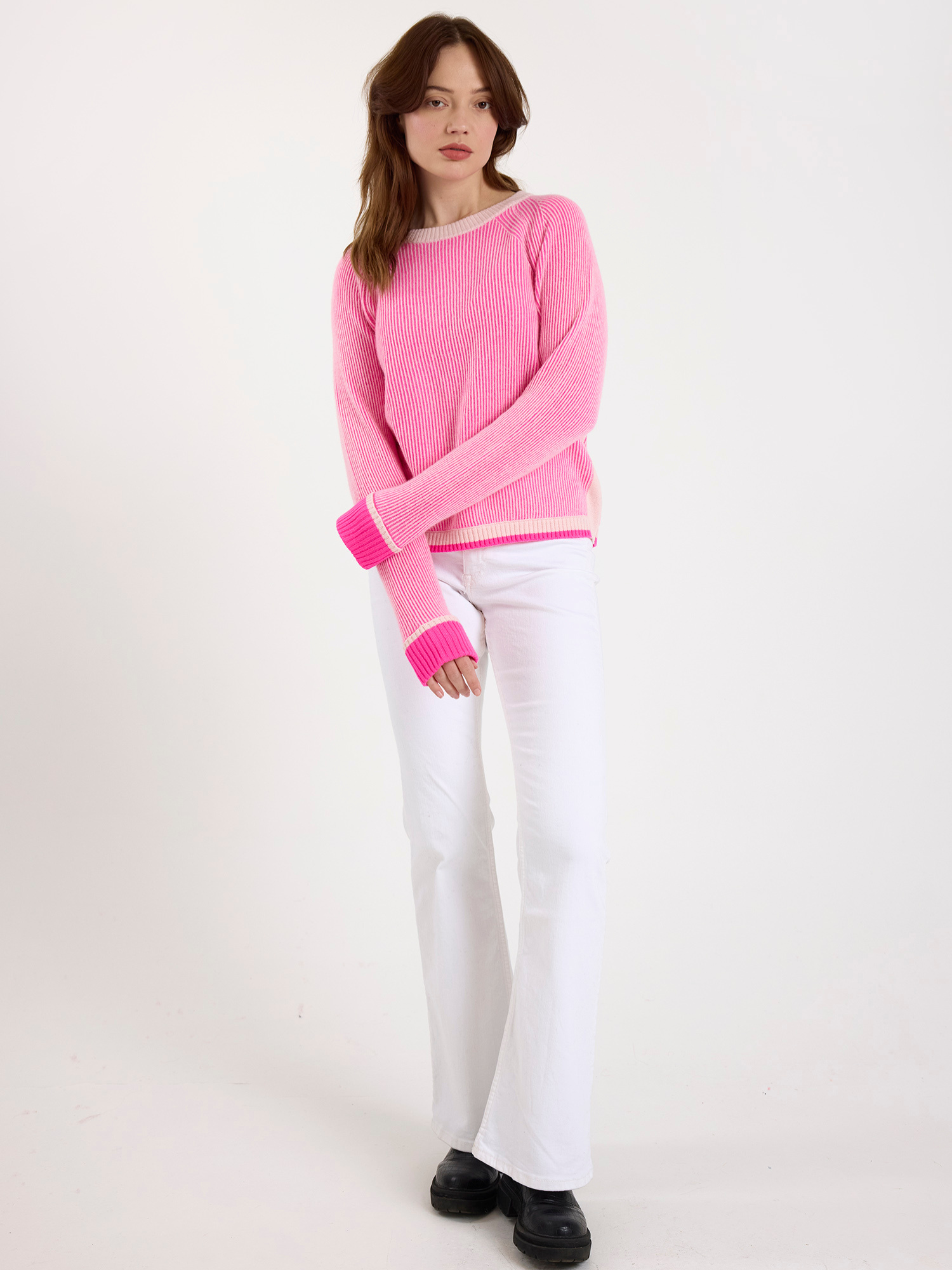 Woman wearing a ribbed pink sweater and white jeans on a white background