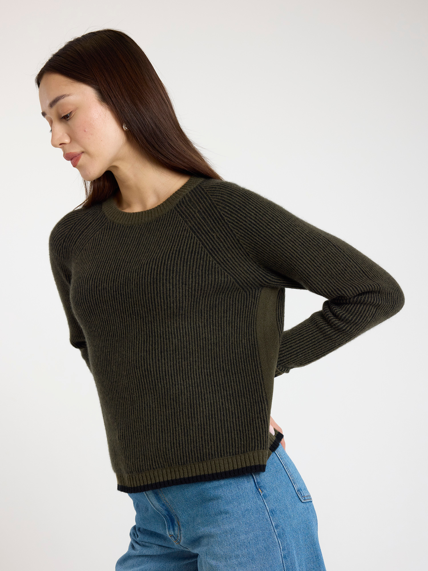 Woman wearing a ribbed dark green sweater and blue jeans on a white background