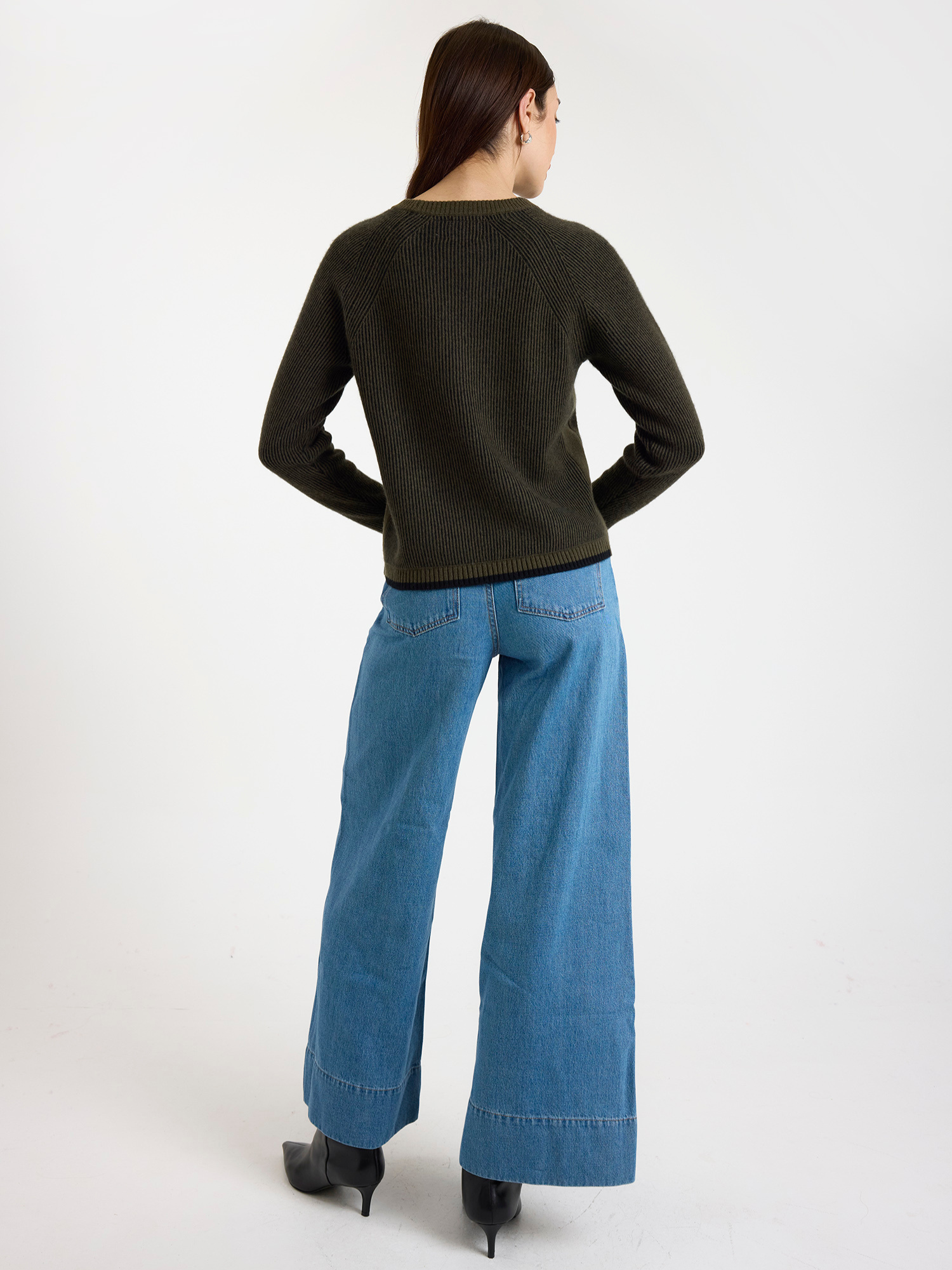 Woman wearing a ribbed dark green sweater and blue jeans on a white background