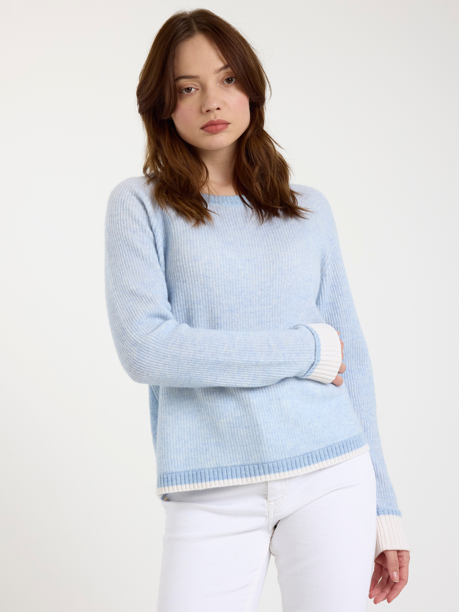 Woman wearing a ribbed light blue sweater with white cuffs and hem on a white background