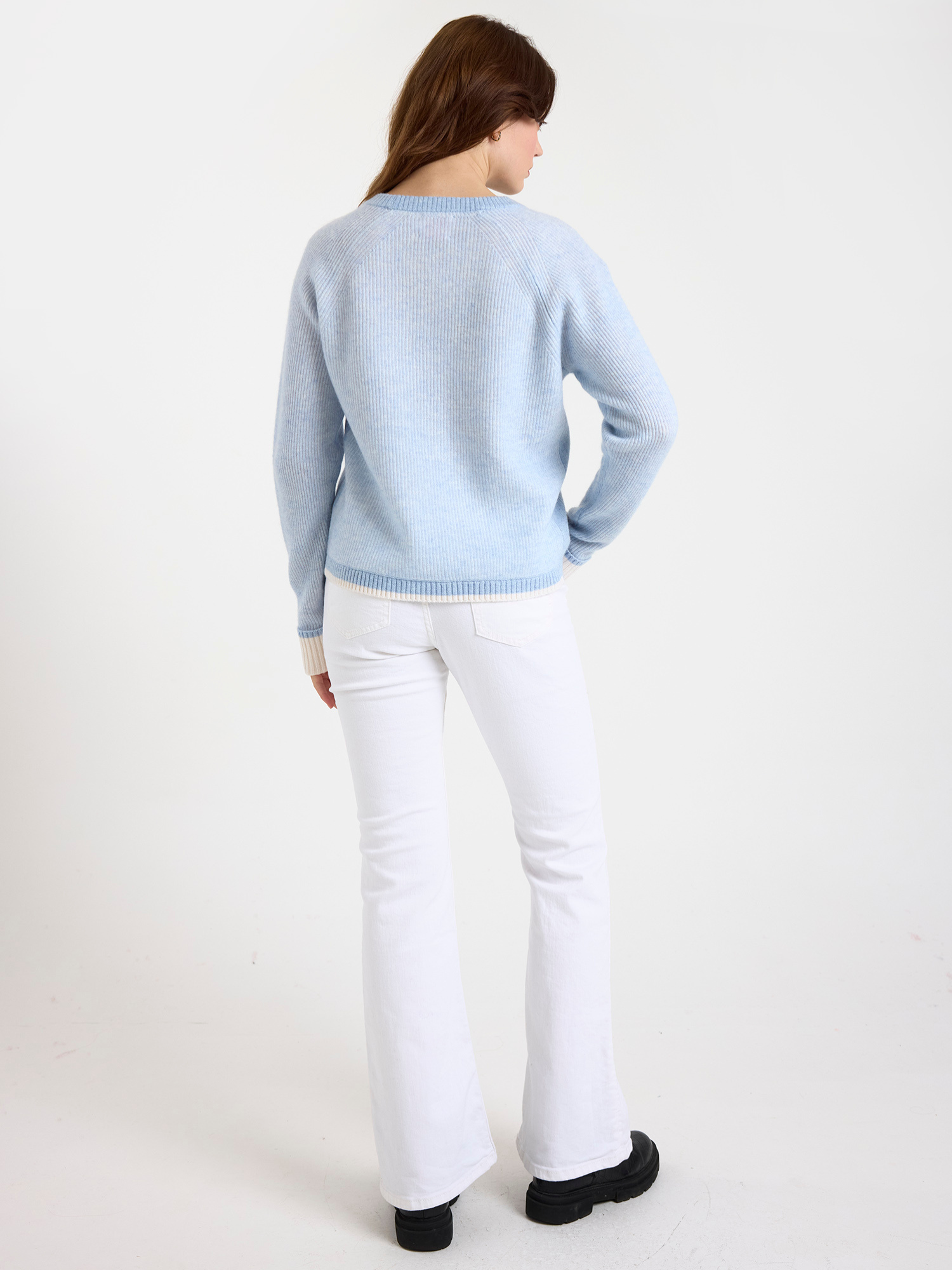 Woman wearing a ribbed light blue sweater and white jeans on a plain background