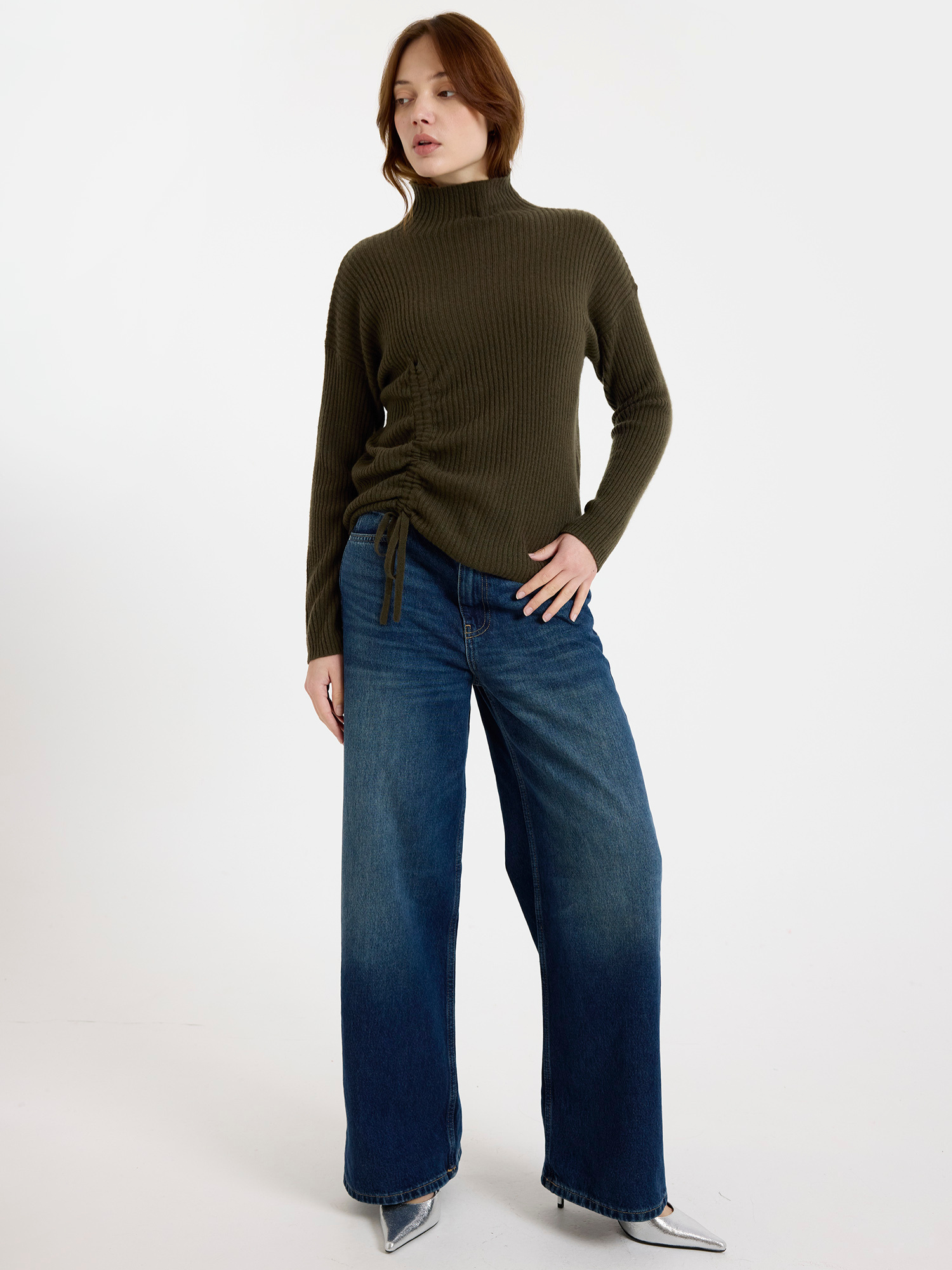 Woman wearing a green ribbed sweater and blue jeans on a white background