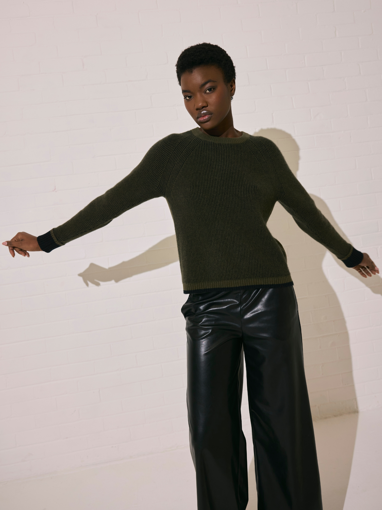 Woman wearing a ribbed dark green sweater and black leather pants against a white background