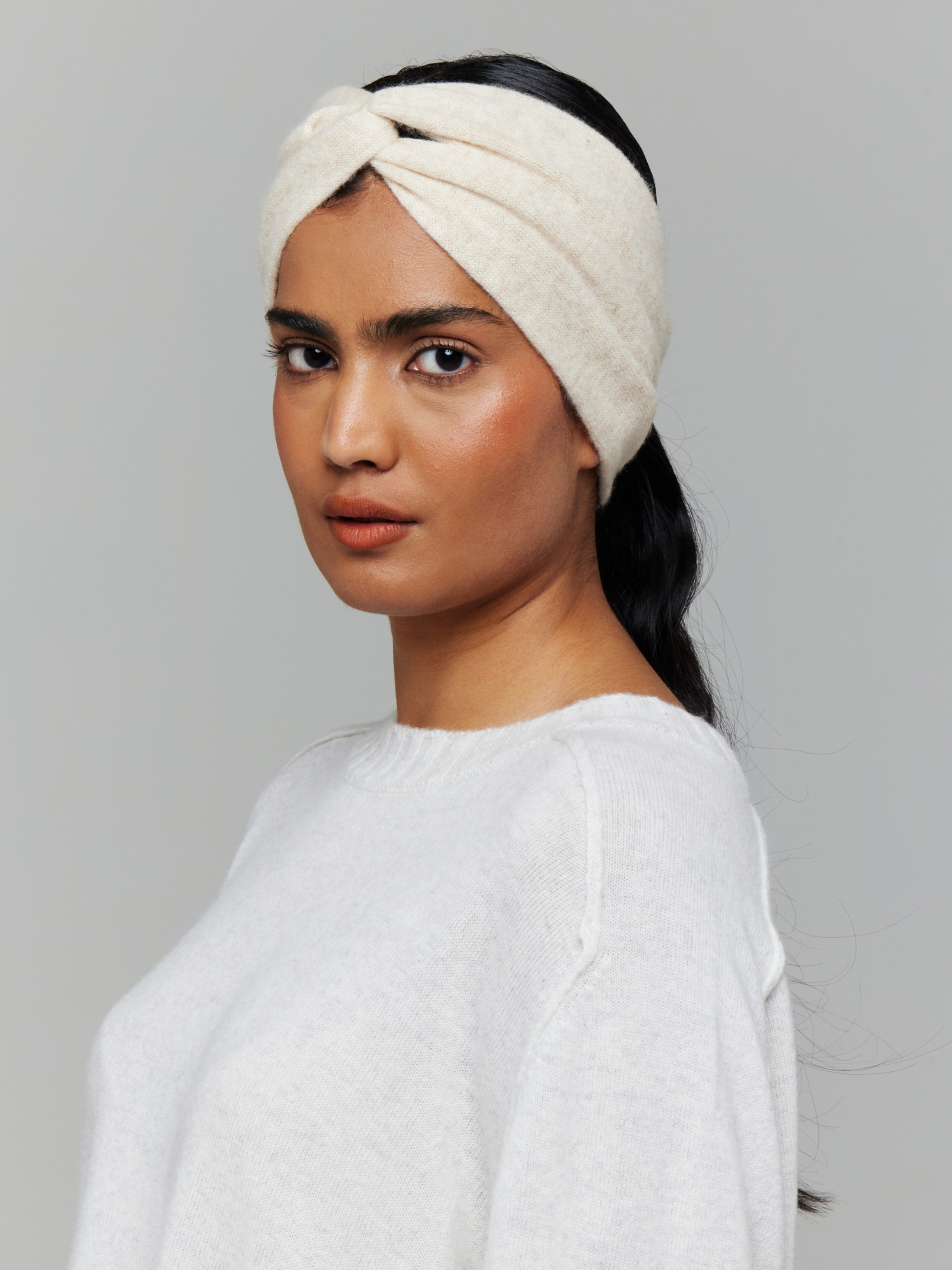 Woman wearing a white knitted headband on a grey background
