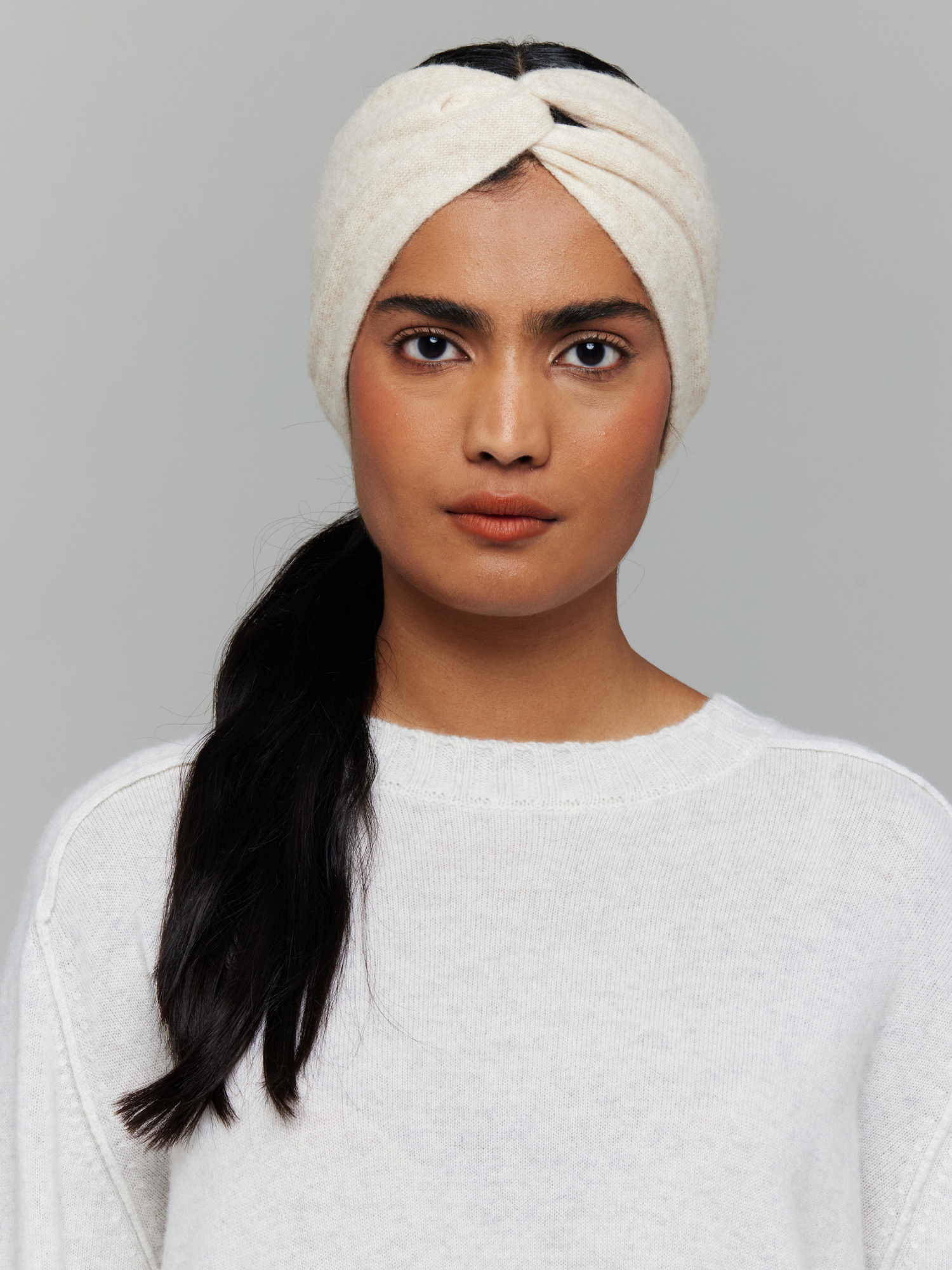 Woman wearing a white knitted headband on a grey background