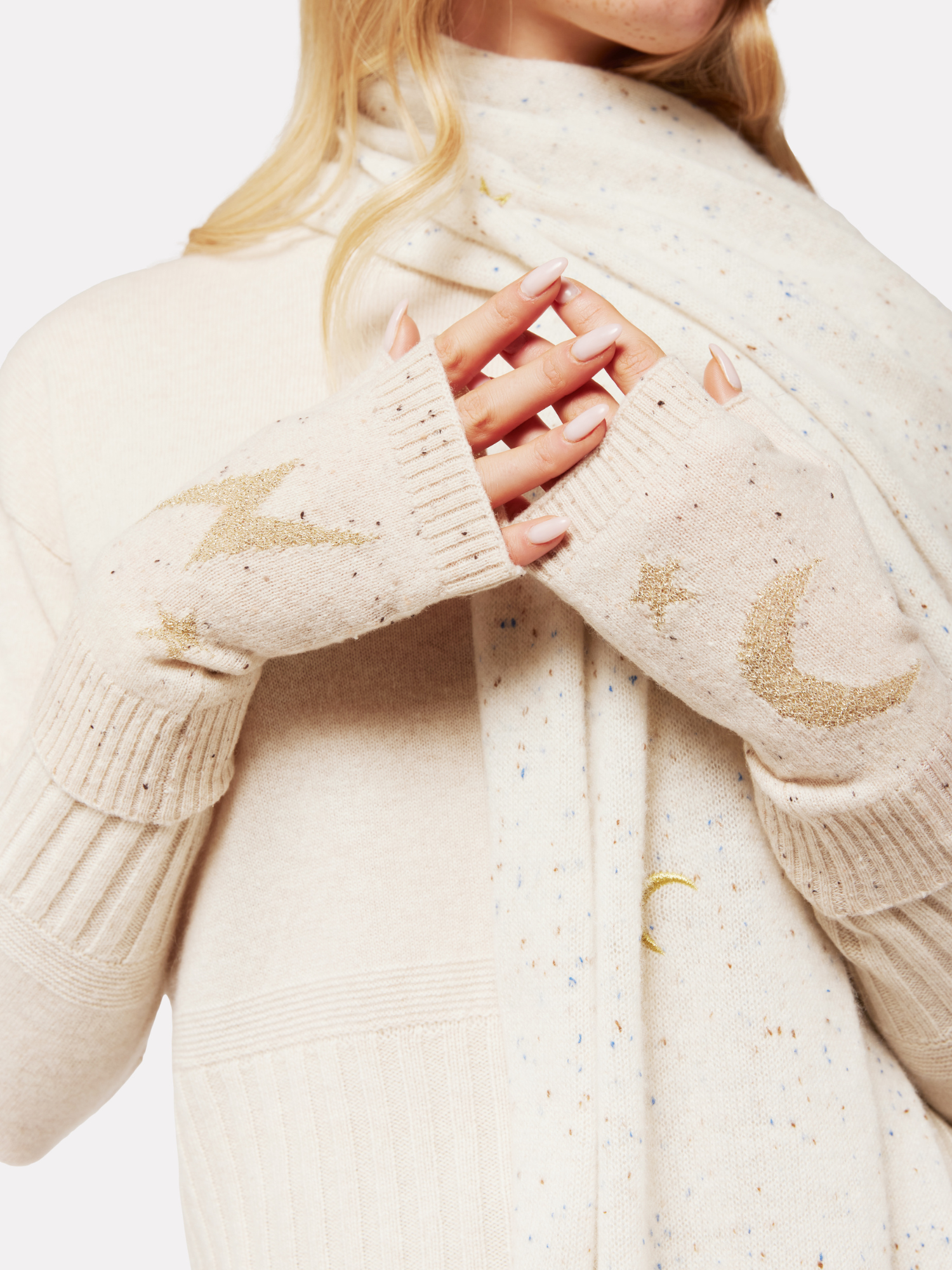 Close-up of a person wearing a cream-colored sweater and wrist warmers with embroidered designs.