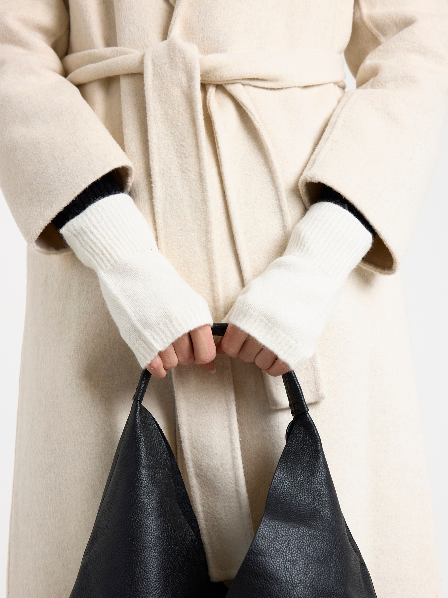 Person wearing a beige coat and white gloves holding a black handbag.