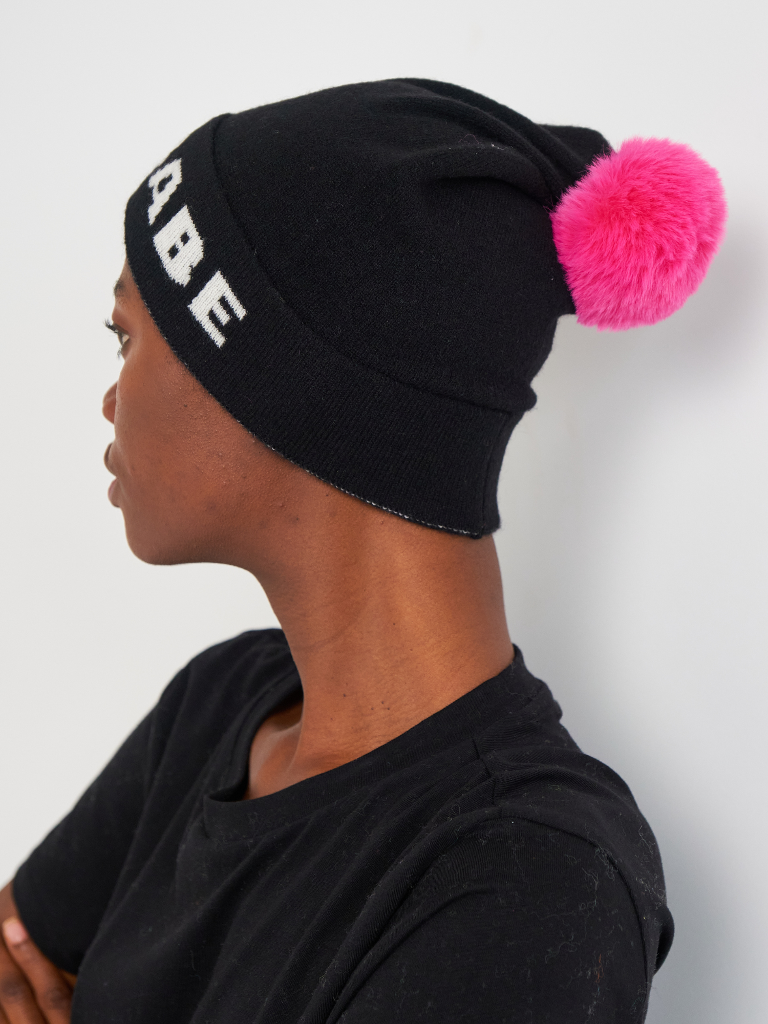 Person wearing a black beanie with a pink pom-pom on a white background