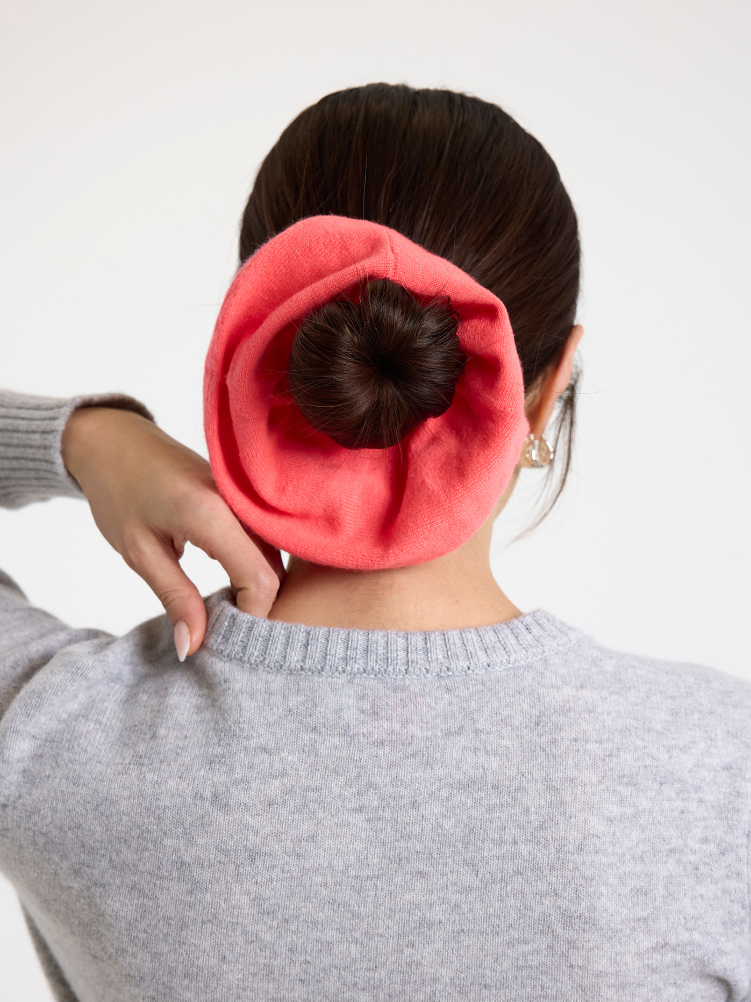 Person wearing a pink scrunchie in their hair on a white background