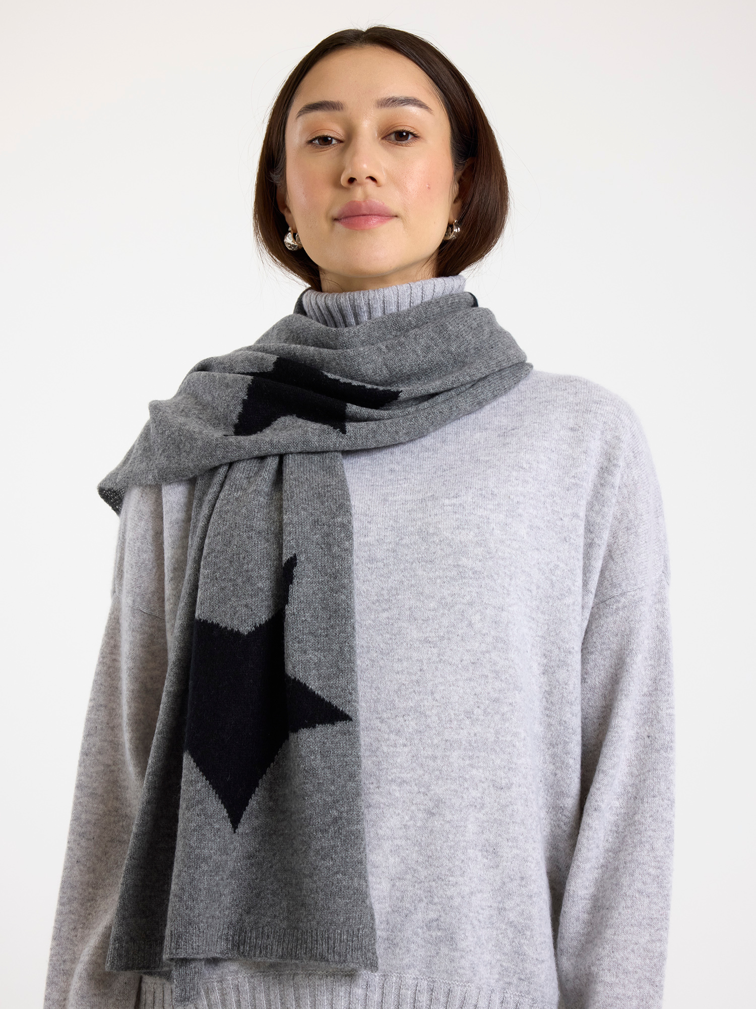Woman wearing a gray sweater and black star-patterned scarf on a white background