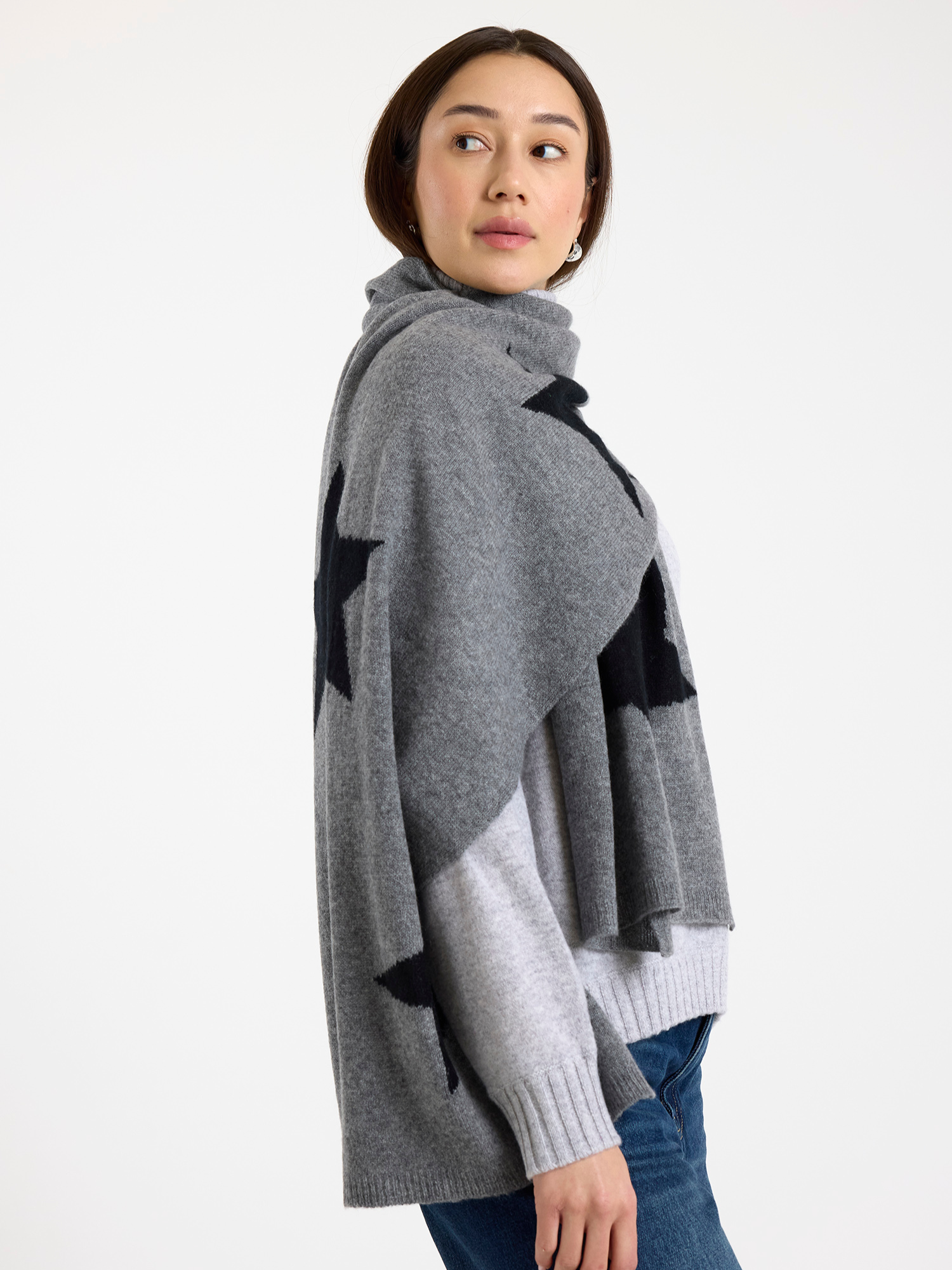 Woman wearing a grey sweater and black star patterned scarf on a white background