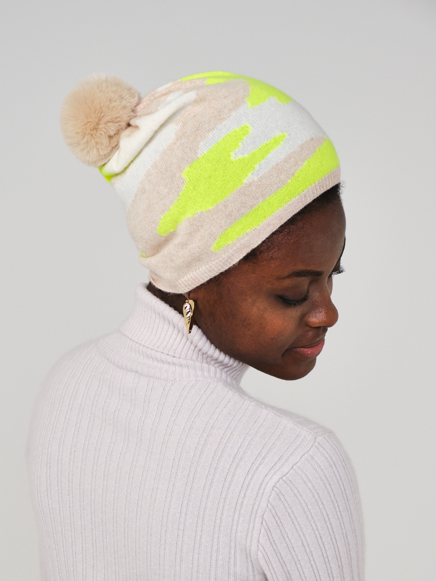 women wearing a beige and yellow camo pattern hat with a pom pom
